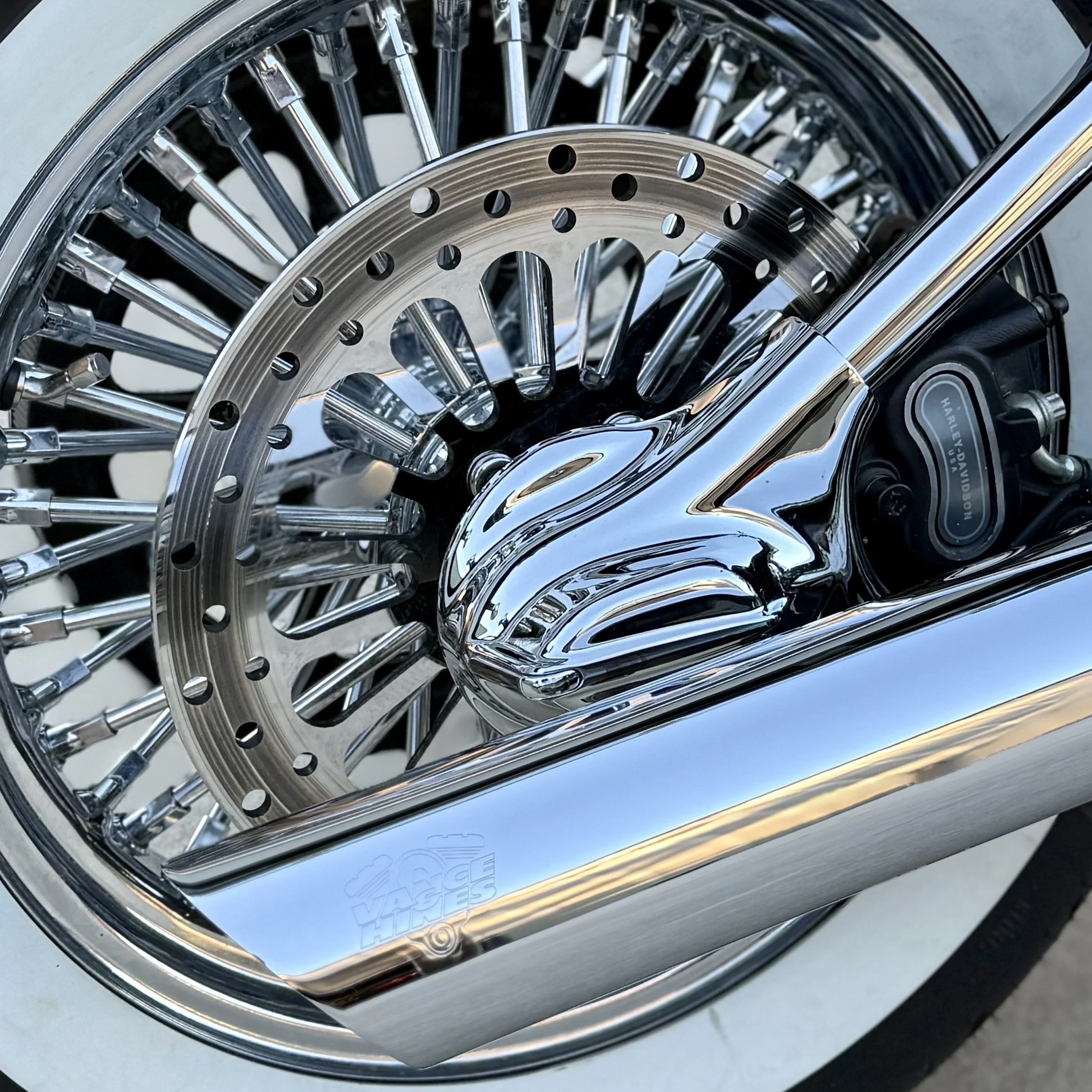 Close-up of a motorcycle wheel, chrome exhaust pipe, and disc brake system.