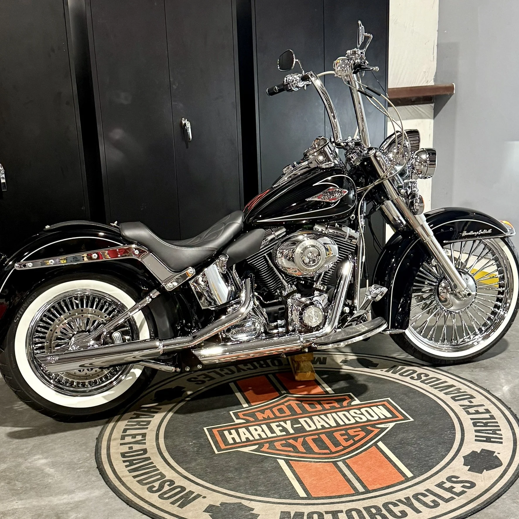 A black Harley-Davidson motorcycle parked on a Harley-Davidson branded mat in a showroom, with black lockers in the background.