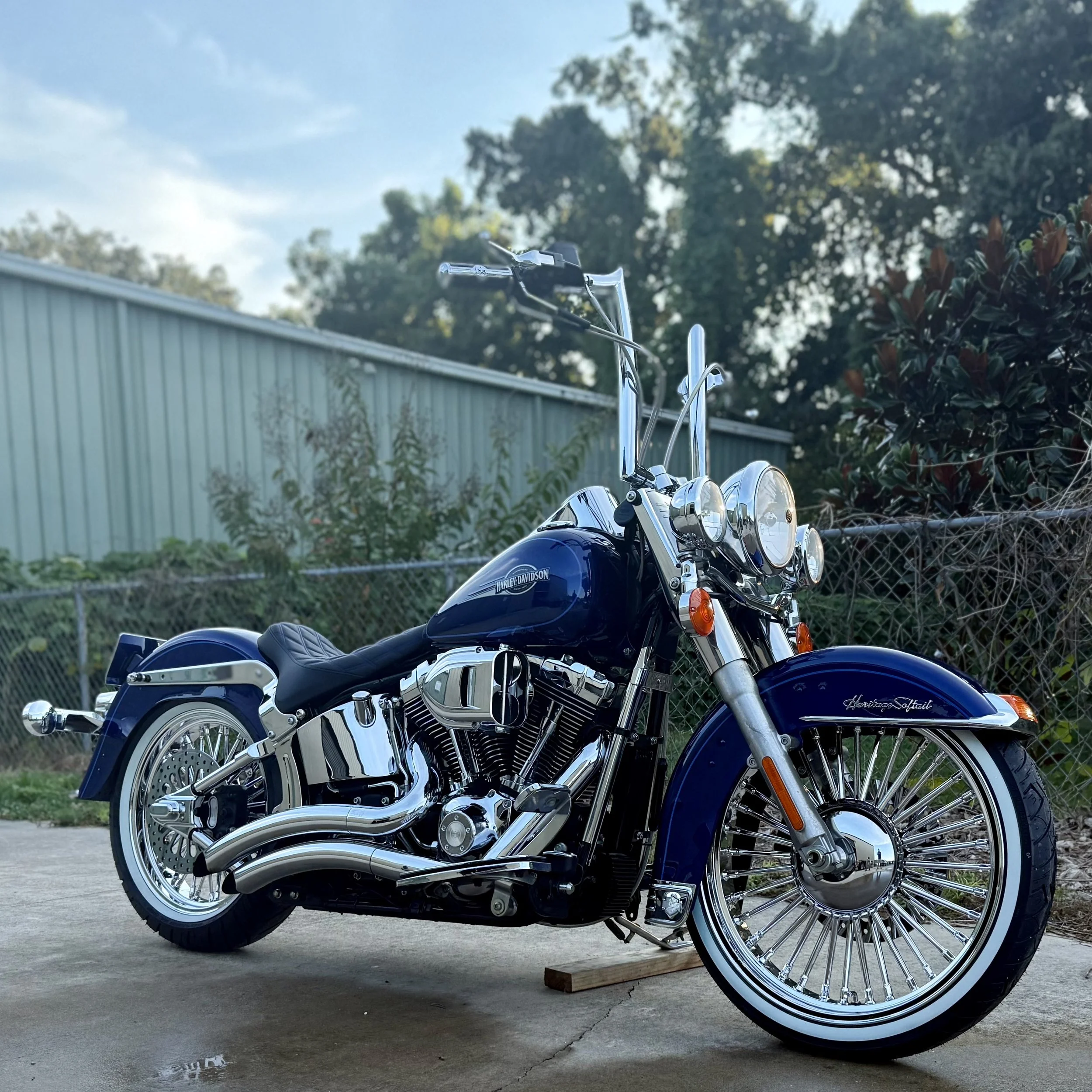 Blue Harley Davidson motorcycle parked on a concrete surface with a fence and greenery in the background.