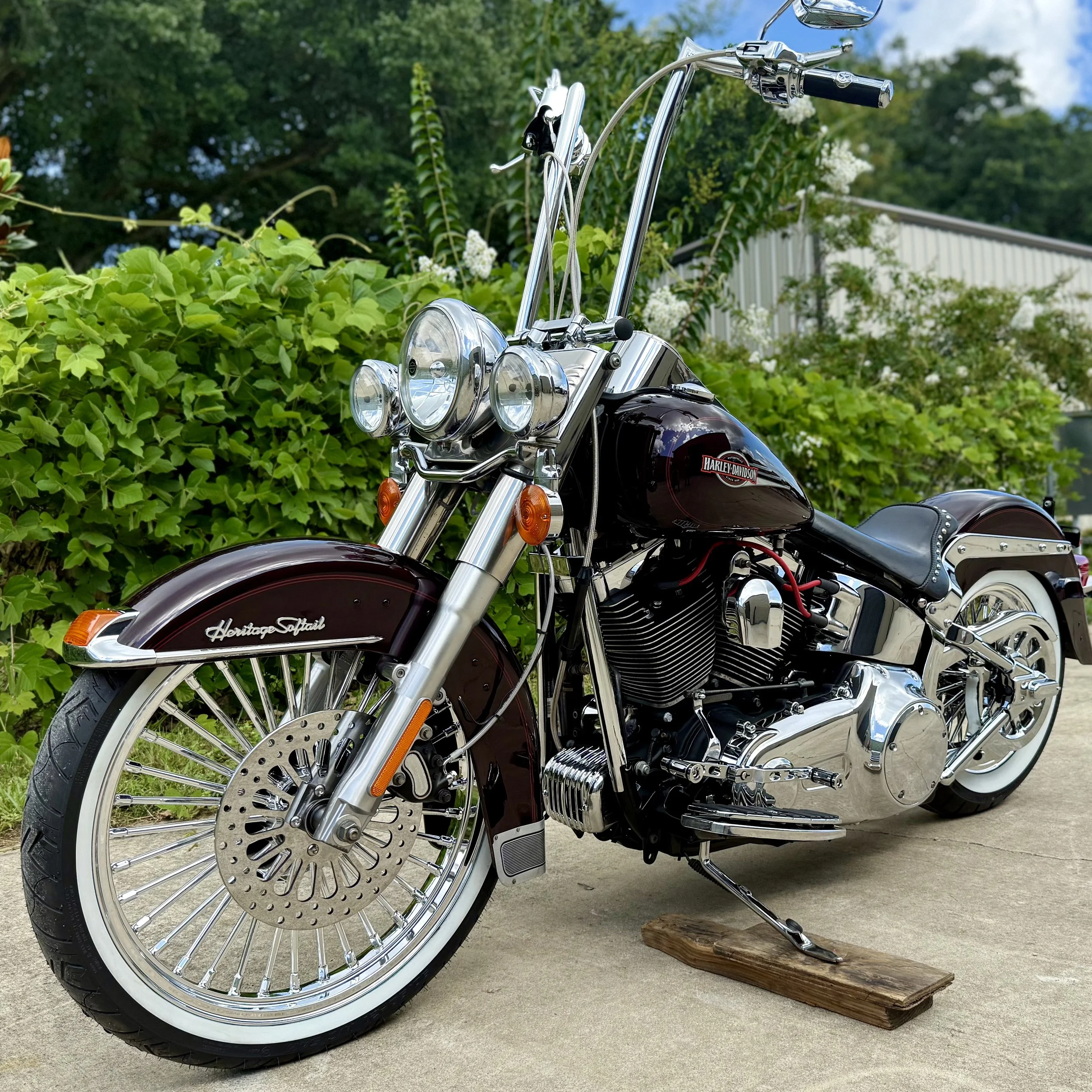 A Harley Davidson Heritage Softail motorcycle parked on a driveway with greenery in the background.