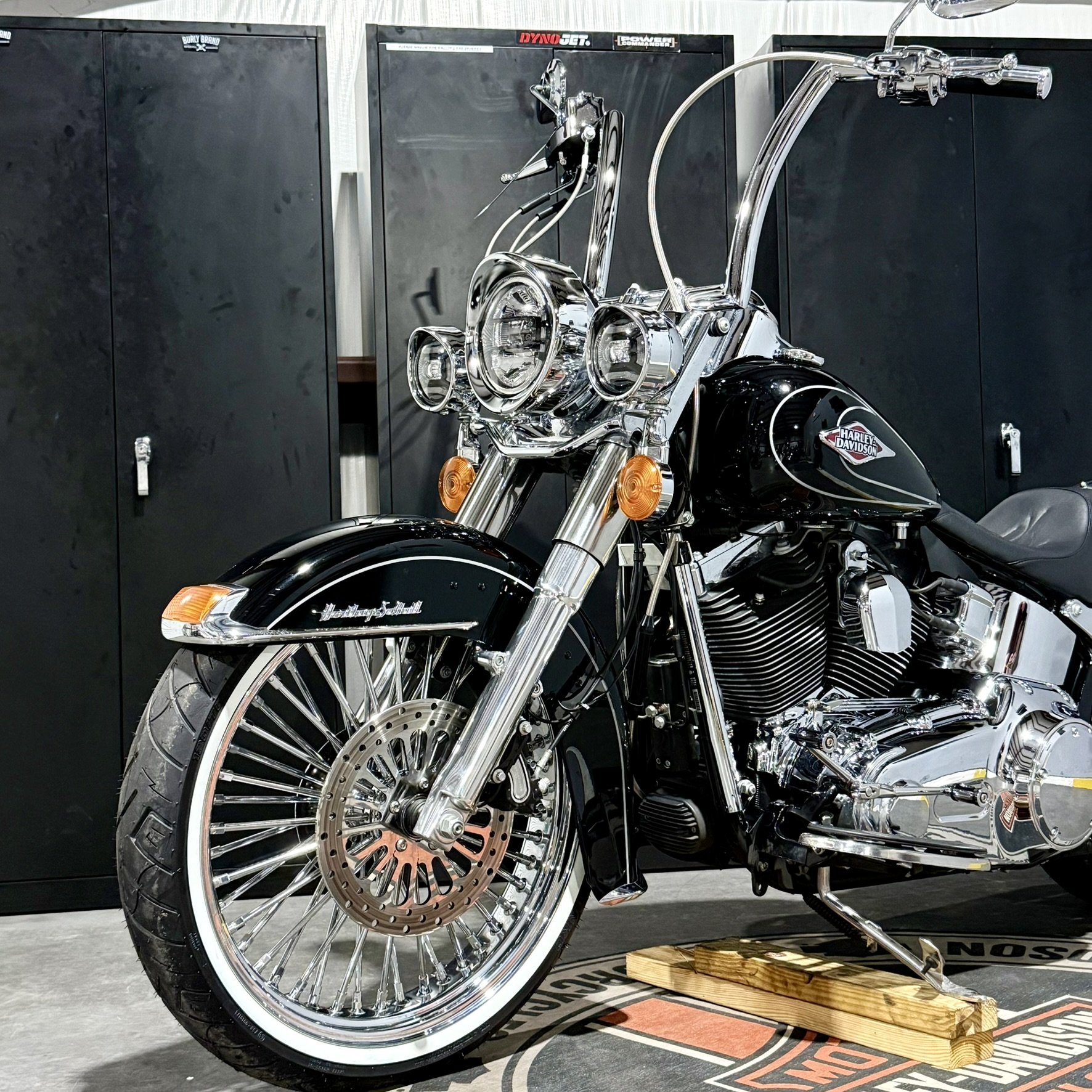 A black Harley Davidson motorcycle with chrome accents, large front wheel, and dual headlights, parked indoors on a wooden block.