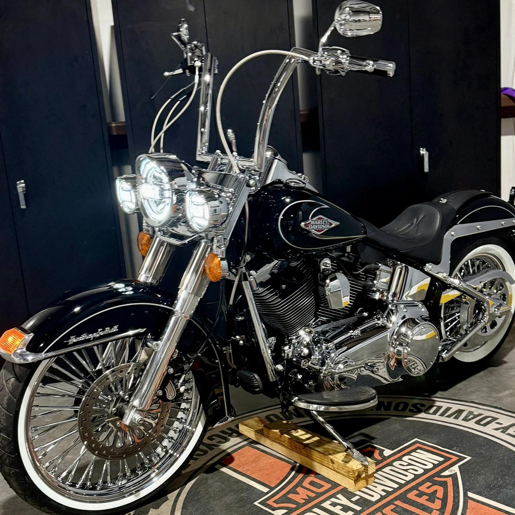 Black Harley Davidson cruiser motorcycle with chrome accents, white-wall tires, and a leather seat, displayed on a Harley Davidson rug.