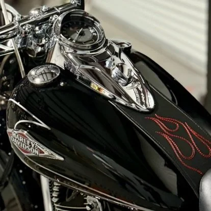 Close-up of a black Harley Davidson motorcycle with chrome details and a leather seat with red stitching.