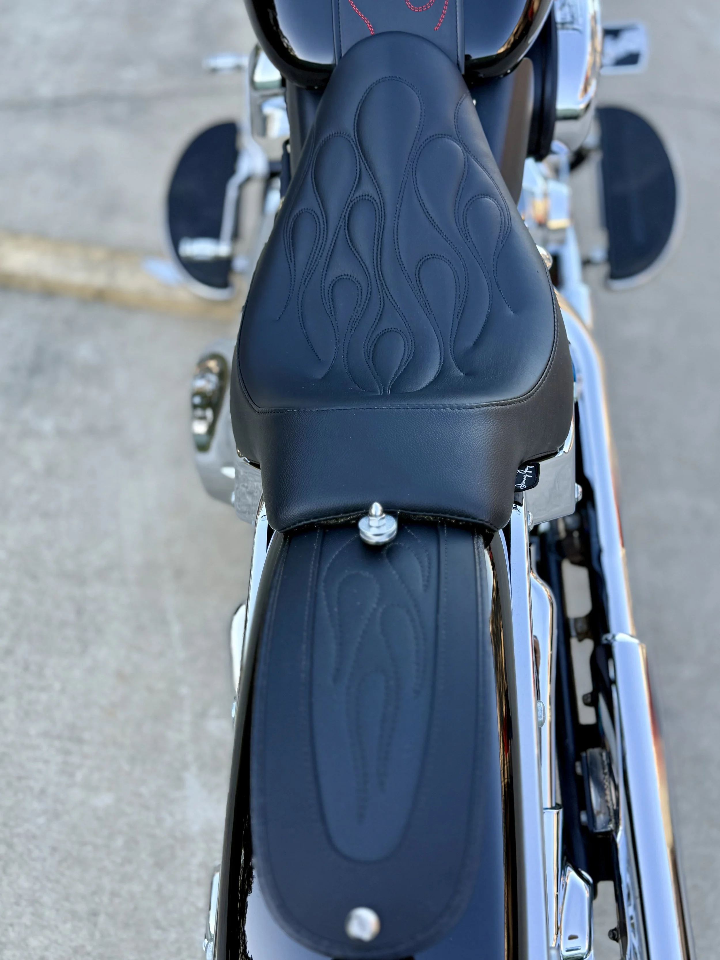 Top view of a black motorcycle seat with flame stitching detail.