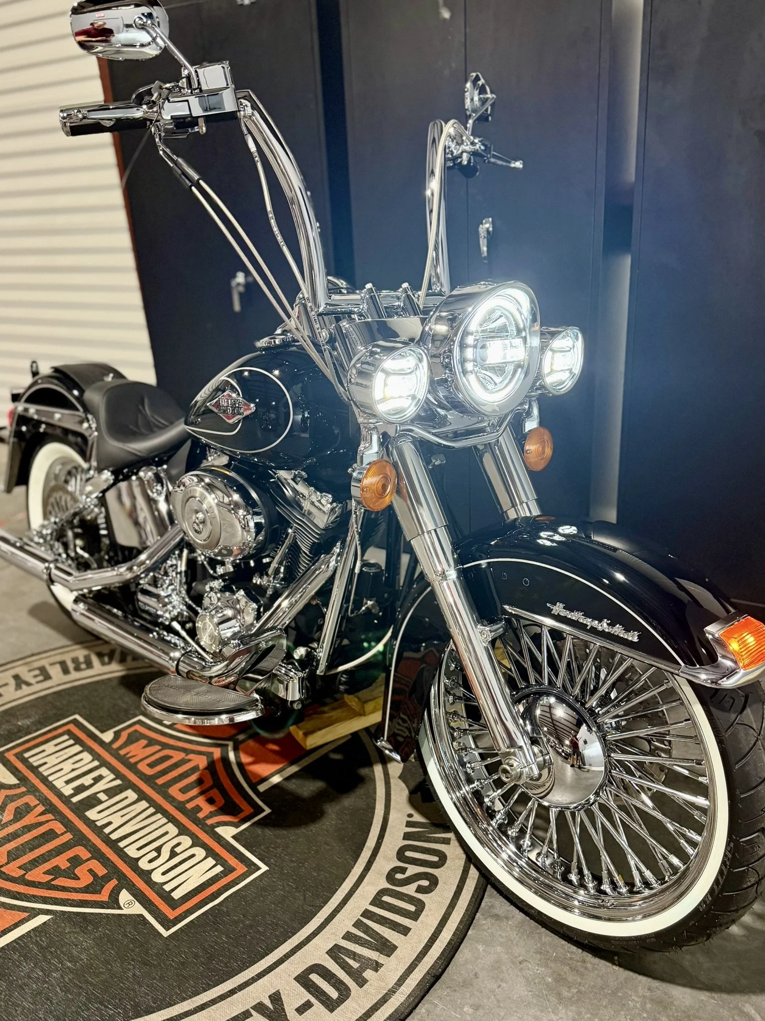 A shiny black Harley-Davidson motorcycle with chrome details on a Harley-Davidson branded floor mat.