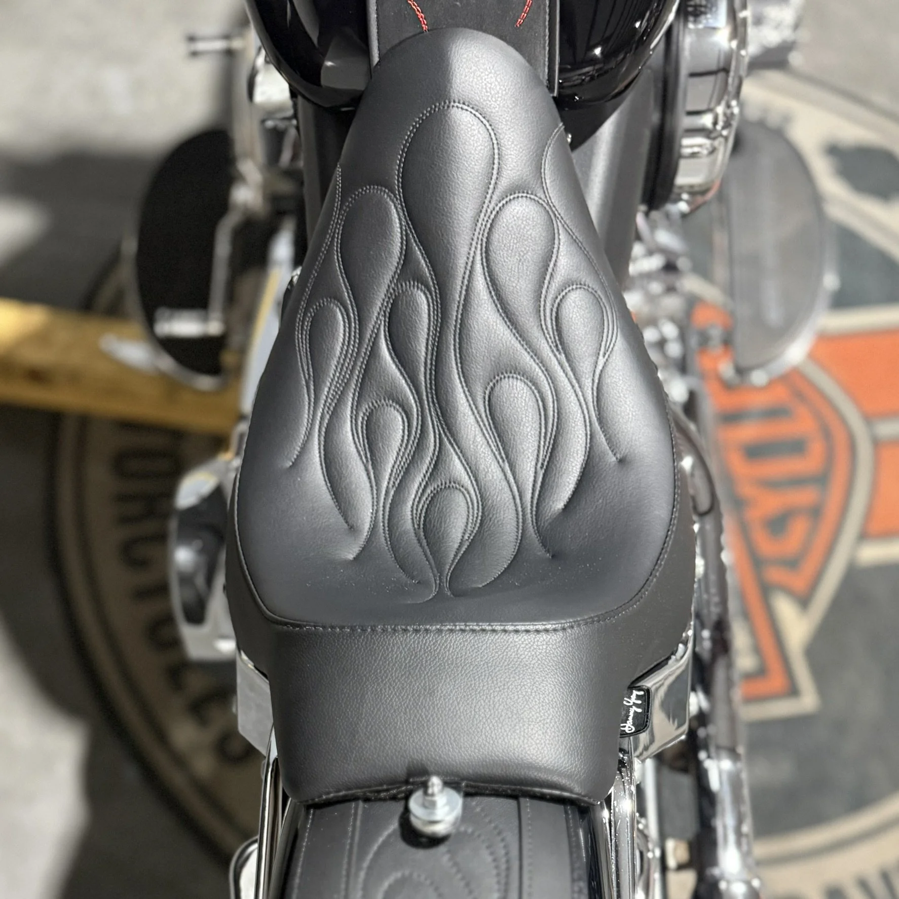 Close-up of a black leather motorcycle seat with flame embroidery stitching.