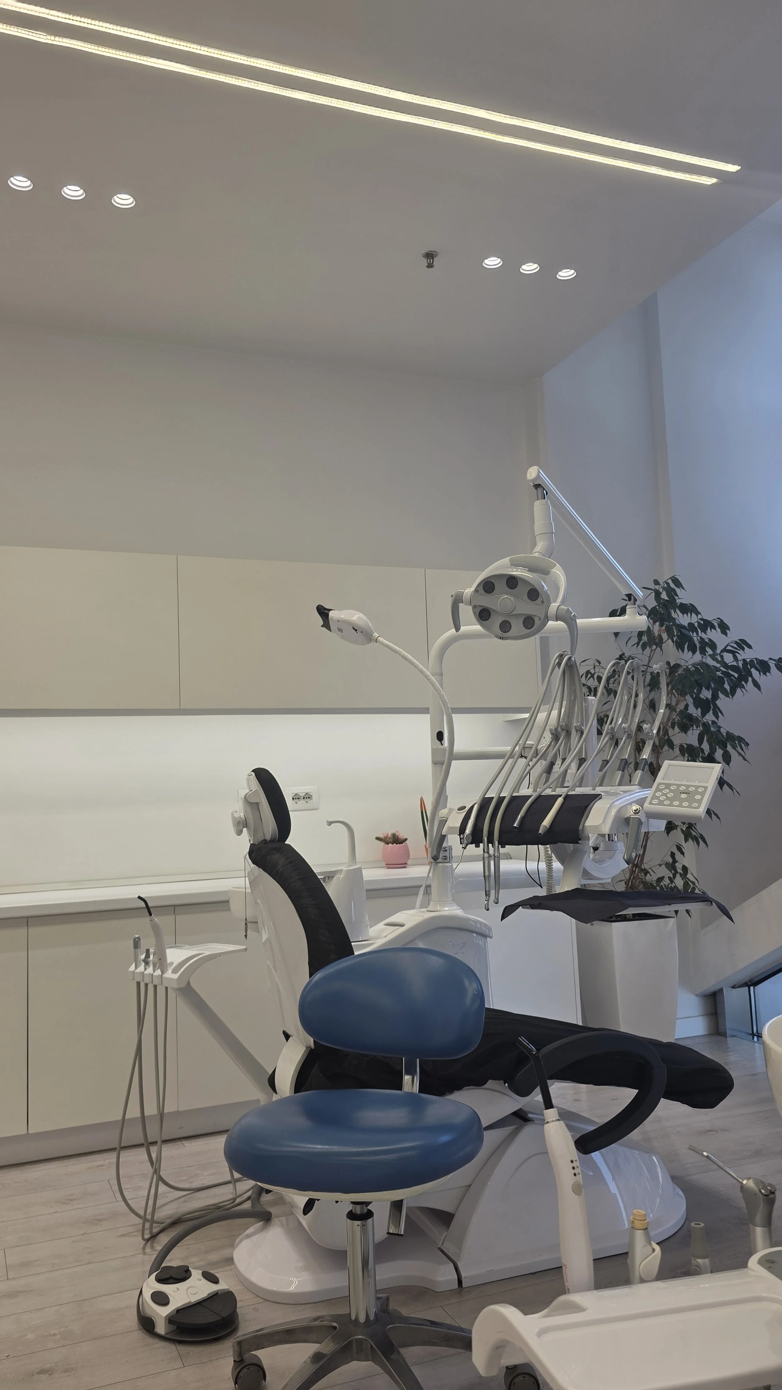 Dental clinic room with dental chair, overhead light, and various dental tools and equipment.