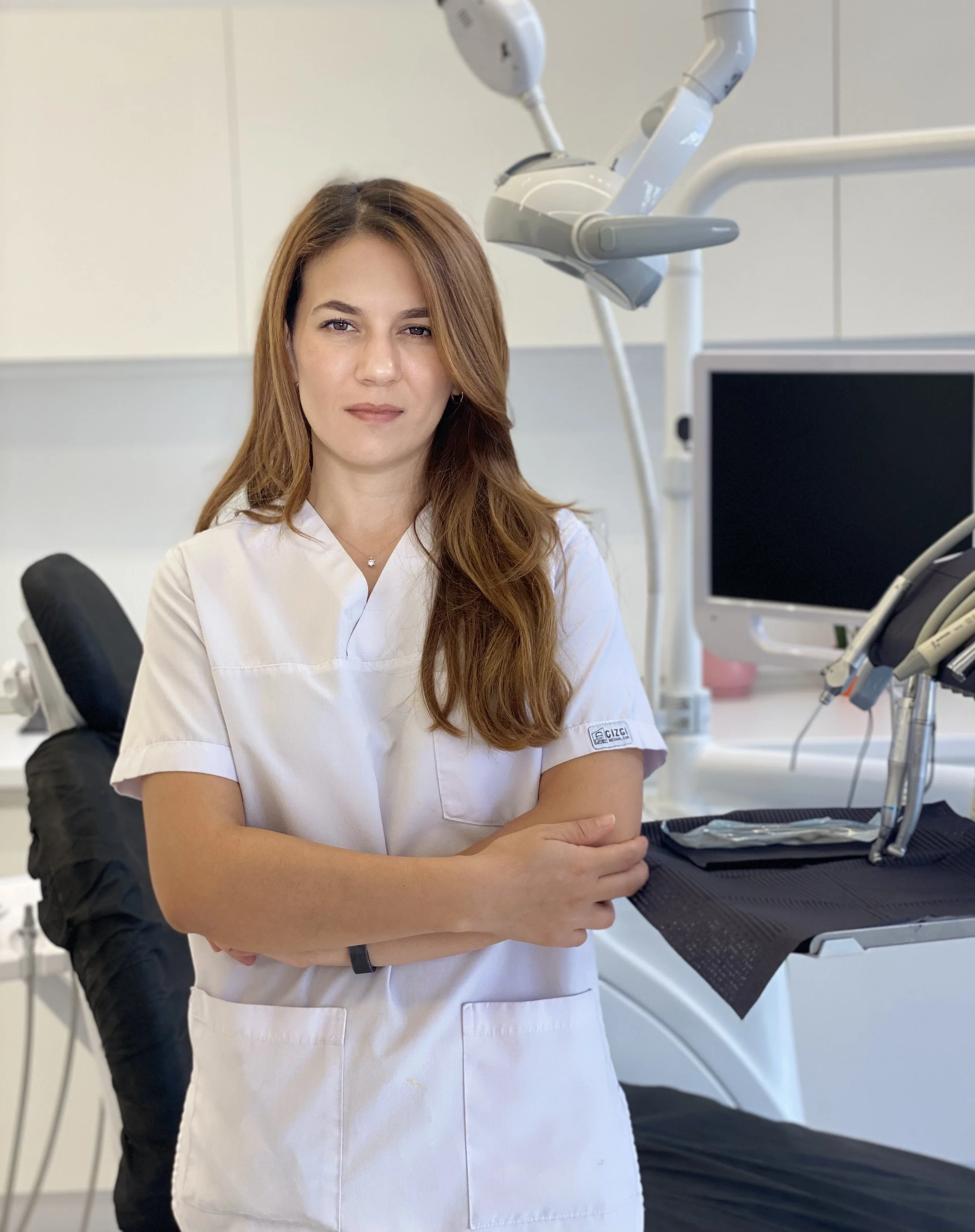 A female dentist posing in a dental clinic with dental tools and equipment around her.