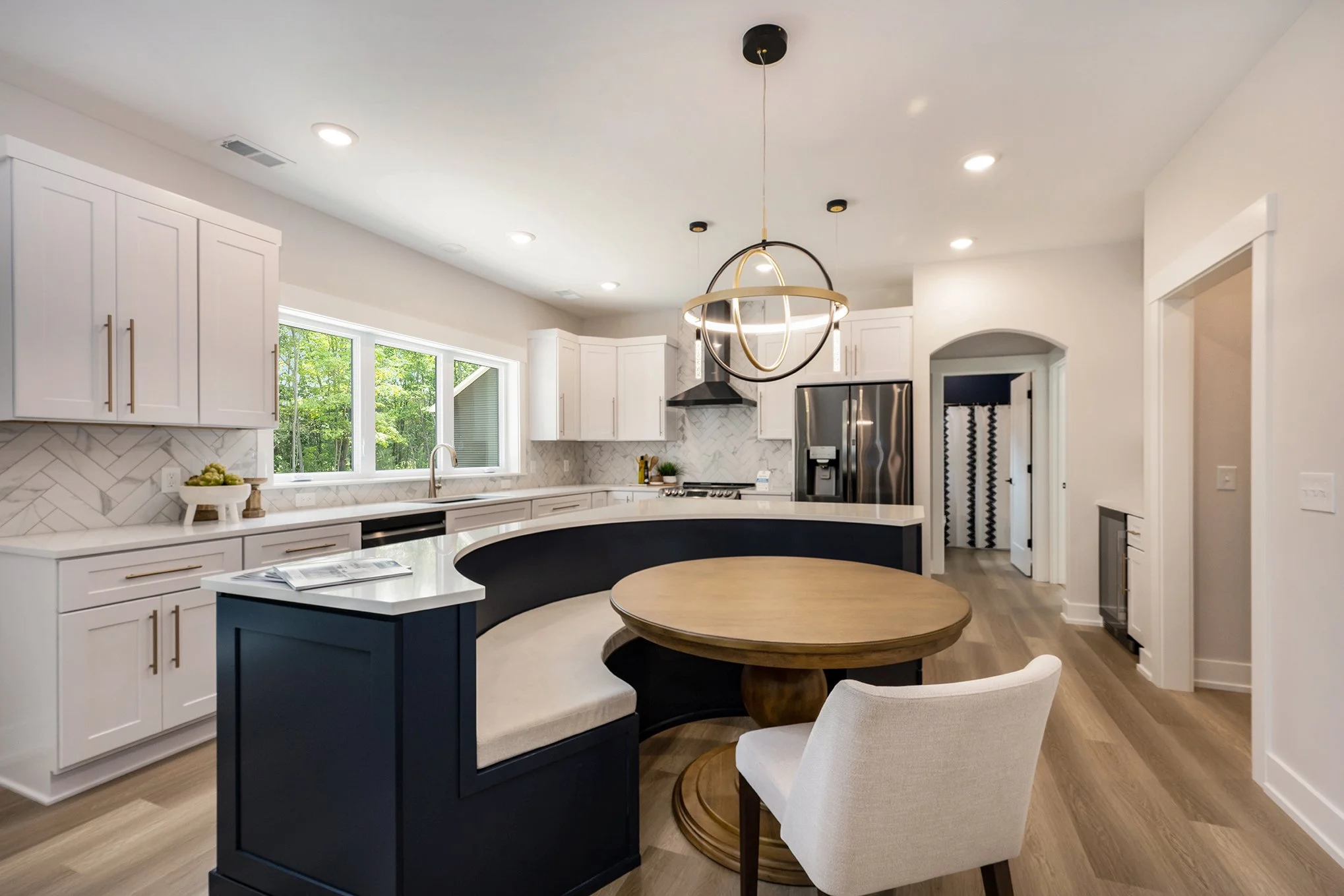 Modern kitchen with white cabinets, a large window, a black and wood dining table, and stainless steel appliances, including a refrigerator and range hood.