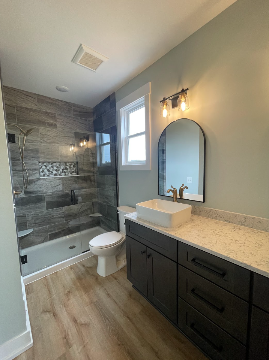 Modern bathroom with a shower, toilet, and vanity with a vessel sink, mirror, and light fixtures.
