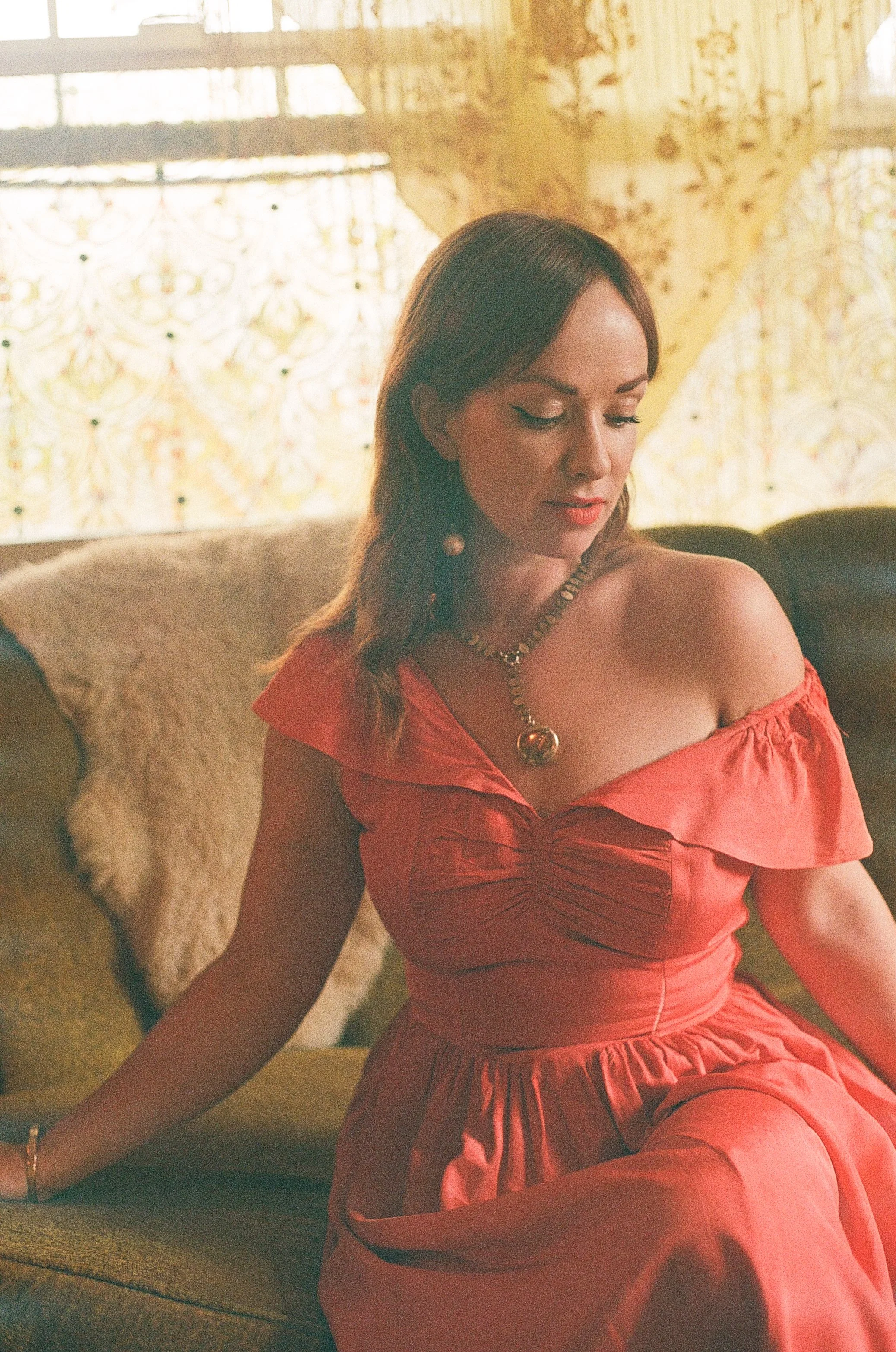A woman in a red off-shoulder dress sitting on a couch with a decorative background and a furry throw pillow.