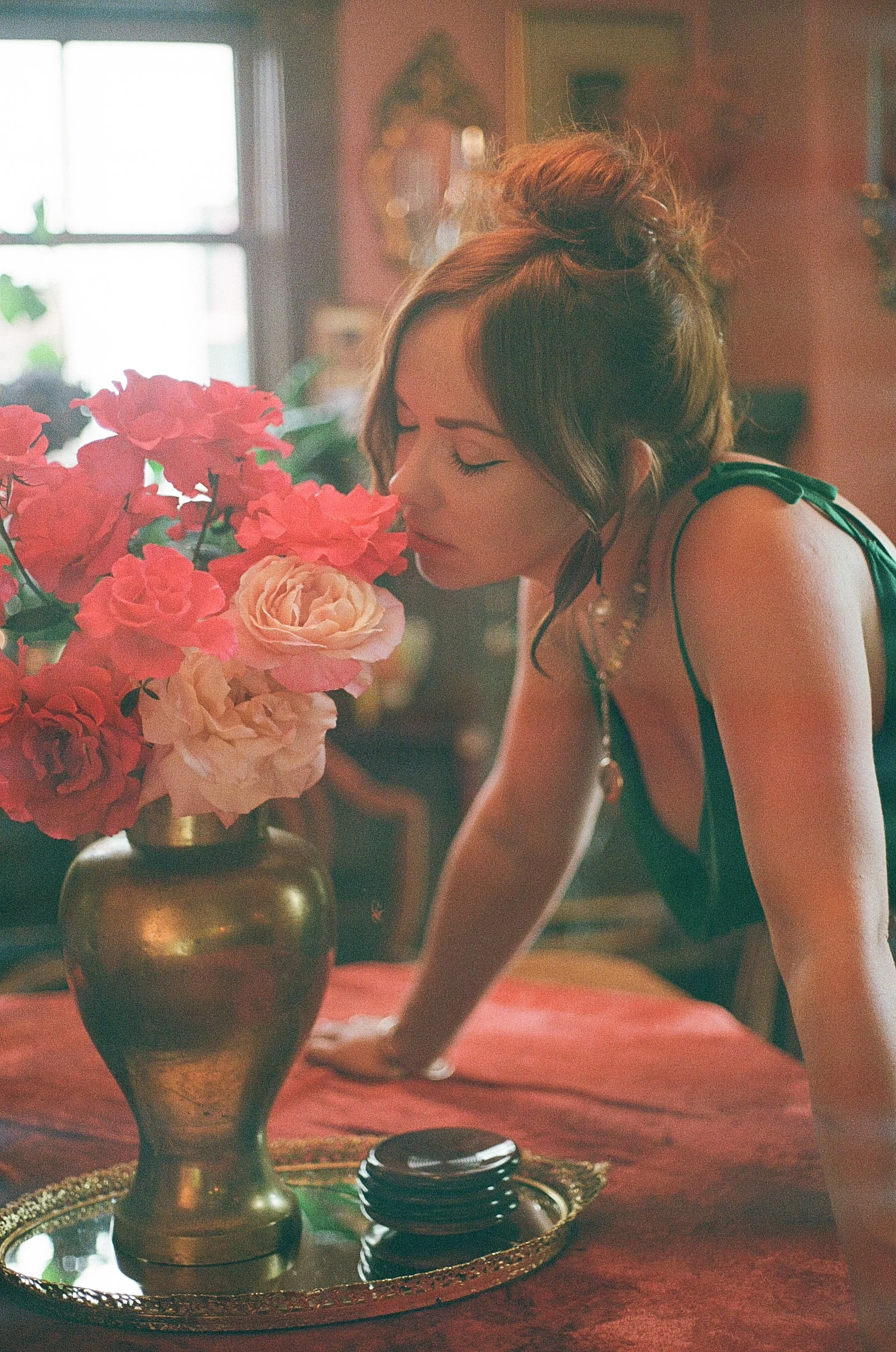 A woman leaning over a table with a large bouquet of pink and white flowers in a gold vase, in a dimly lit room.