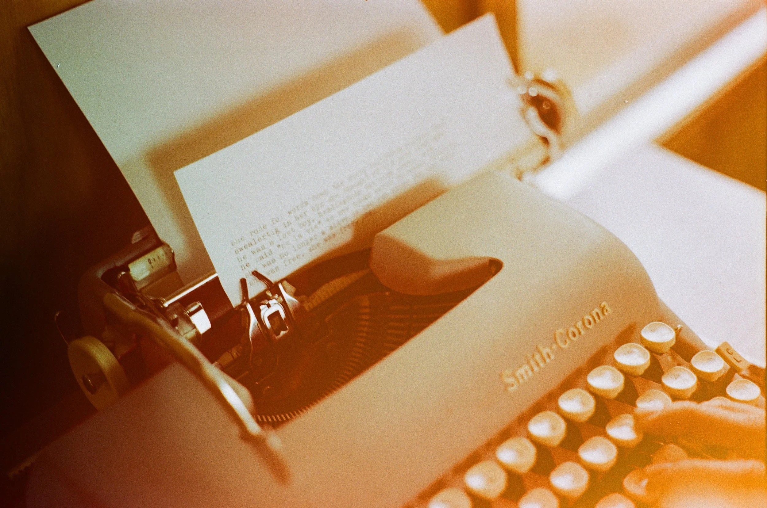 A vintage Smith-Corona typewriter with a sheet of paper inserted, positioned on a table with sunlight illuminating it.