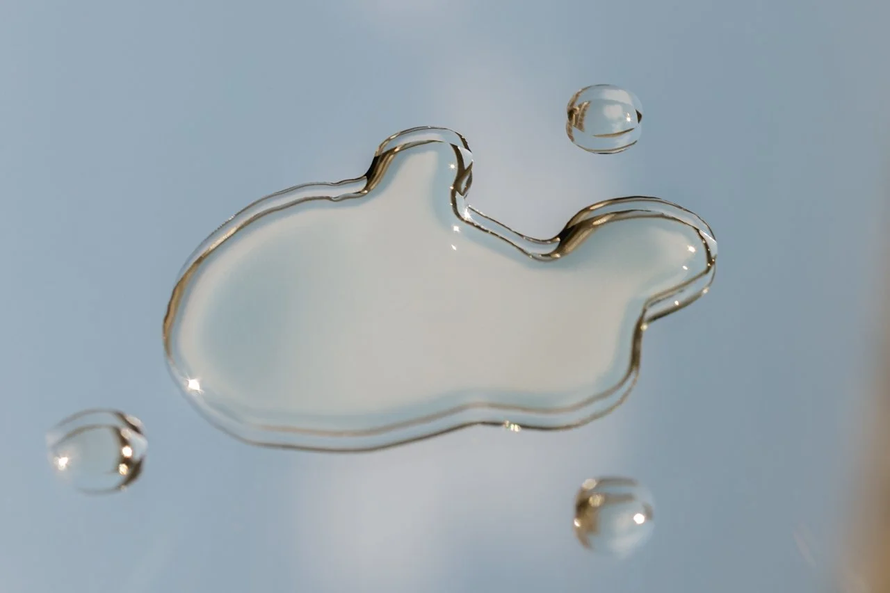 Close-up of a water droplet splashing, with reflections on its surface and a background of soft, cloudy sky.