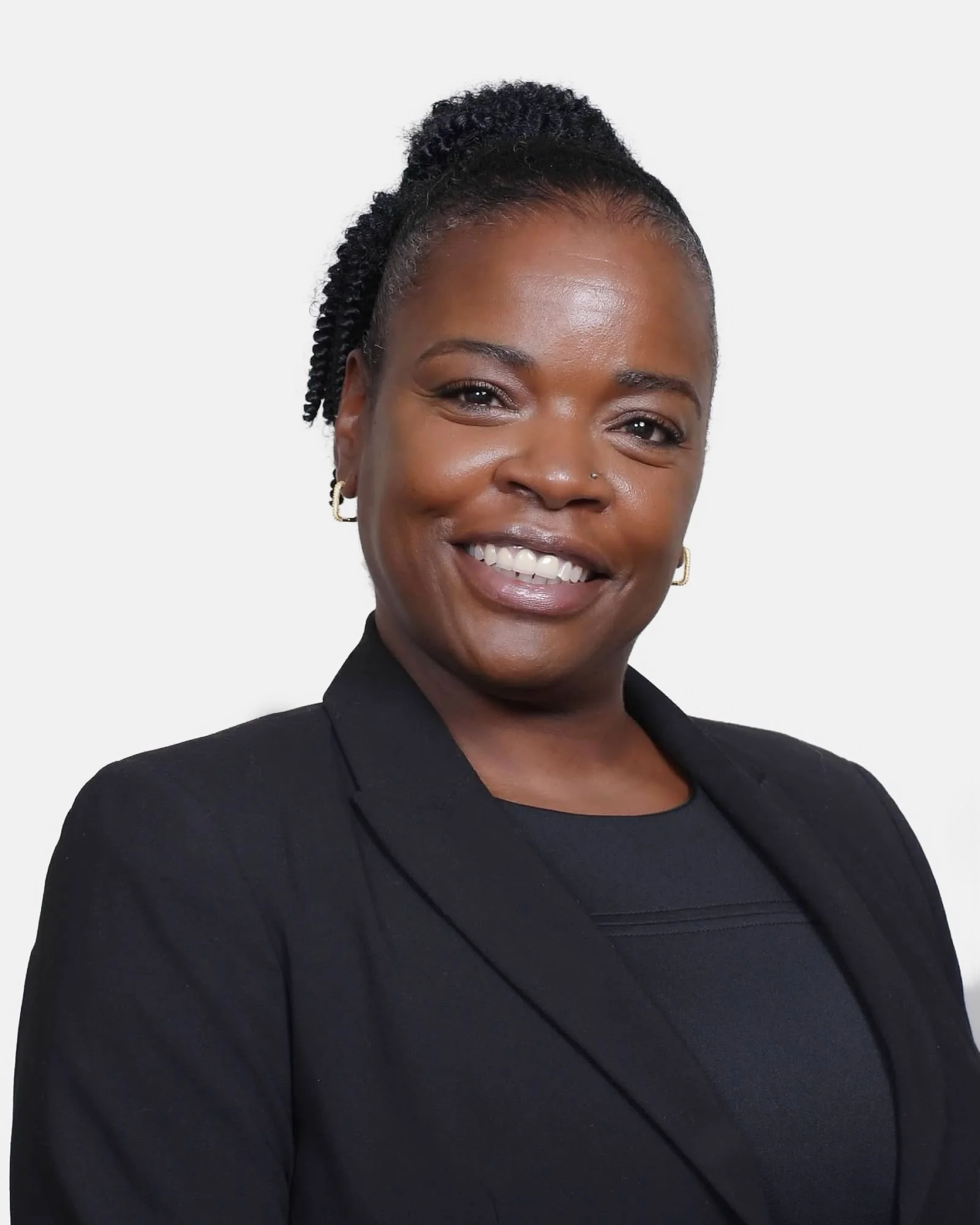 Portrait of a smiling African American woman with natural hair styled in twists, wearing a black blazer and top, against a plain white background.
