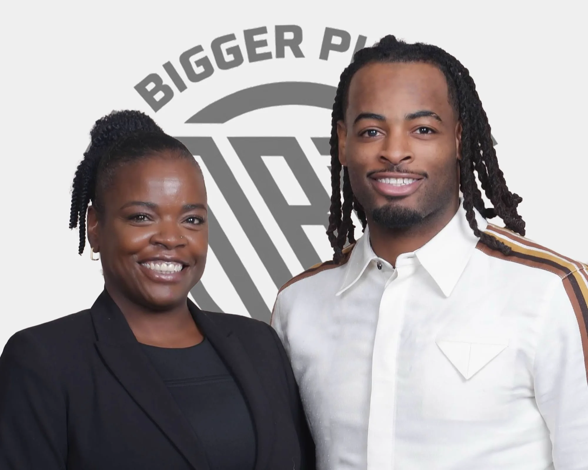 Two smiling individuals, a woman on the left wearing a black blazer and a man on the right with a white shirt featuring striped shoulder accents, standing in front of a background with a logo that says 'Bigger Pyramids'.