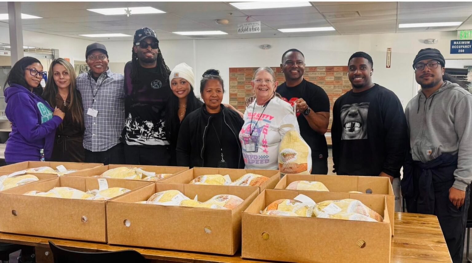 Group of eleven people standing behind tables filled with boxes of food, smiling at the camera in an indoor room.