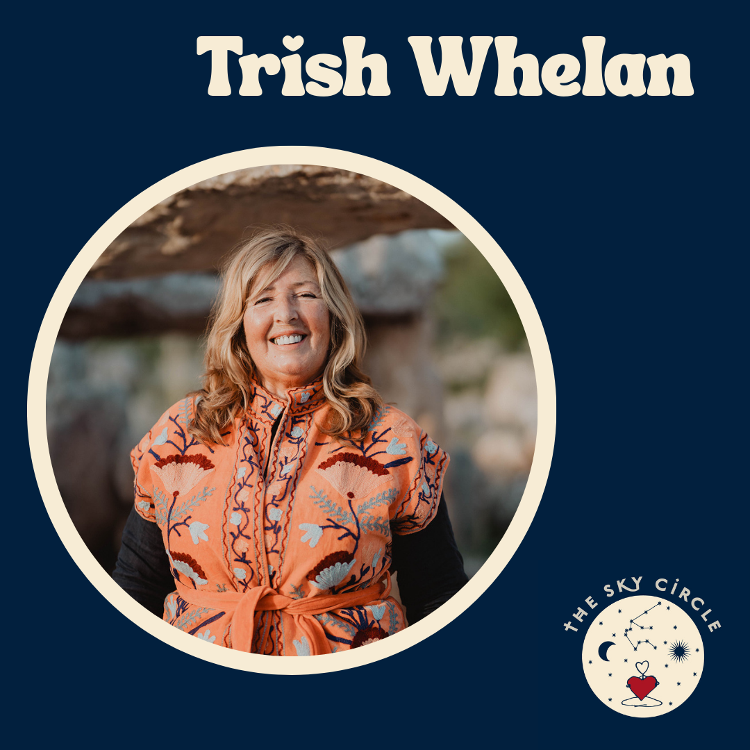 A woman smiling outdoors, wearing a colorful embroidered top with a tied waist, with a nature background.