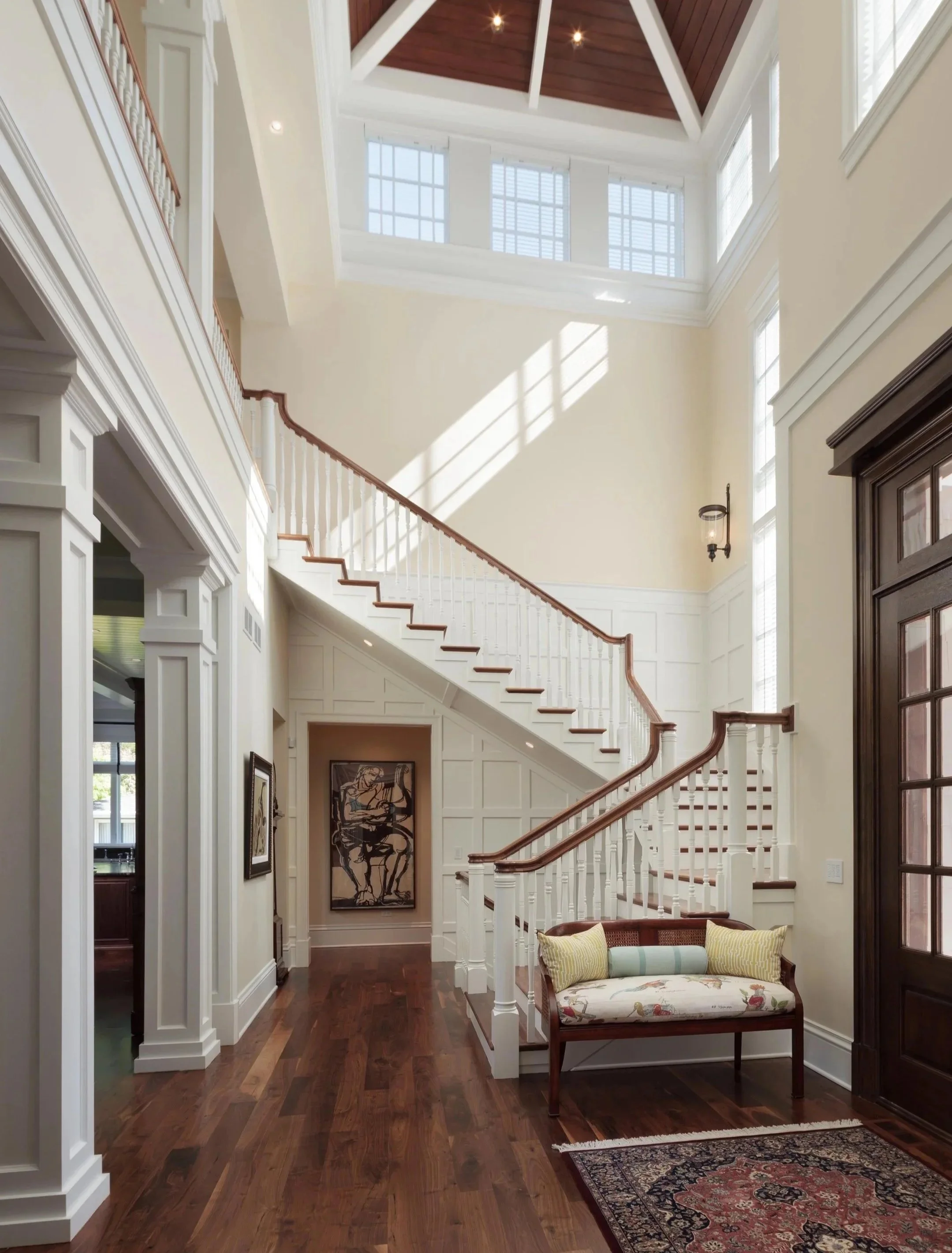 A spacious, well-lit foyer with a staircase, hardwood floors, and a decorative bench against the wall.