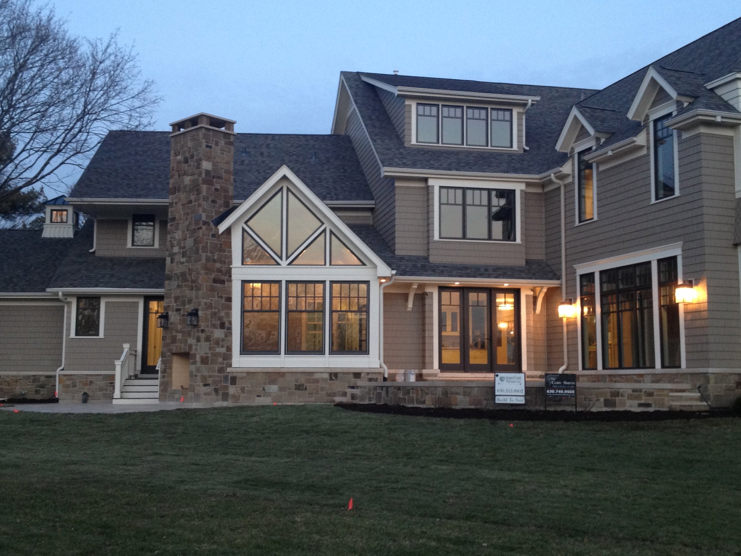 Large multi-story house with stone chimney, multiple windows, and a well-maintained lawn at dusk.
