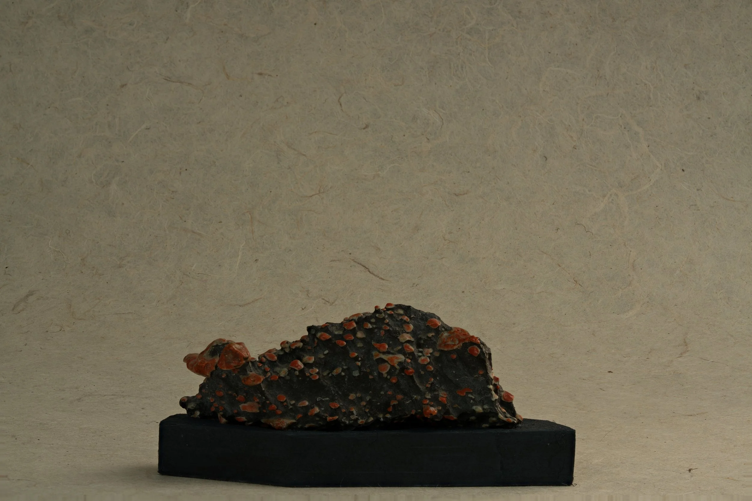 A rock with red and orange patches on a black base, placed on a black rectangular stand.
