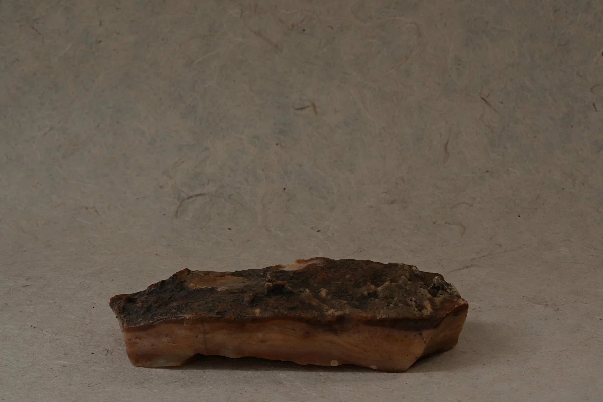 A rough, irregularly shaped rock with shades of brown and reddish tones, placed on a flat surface with a plain background.