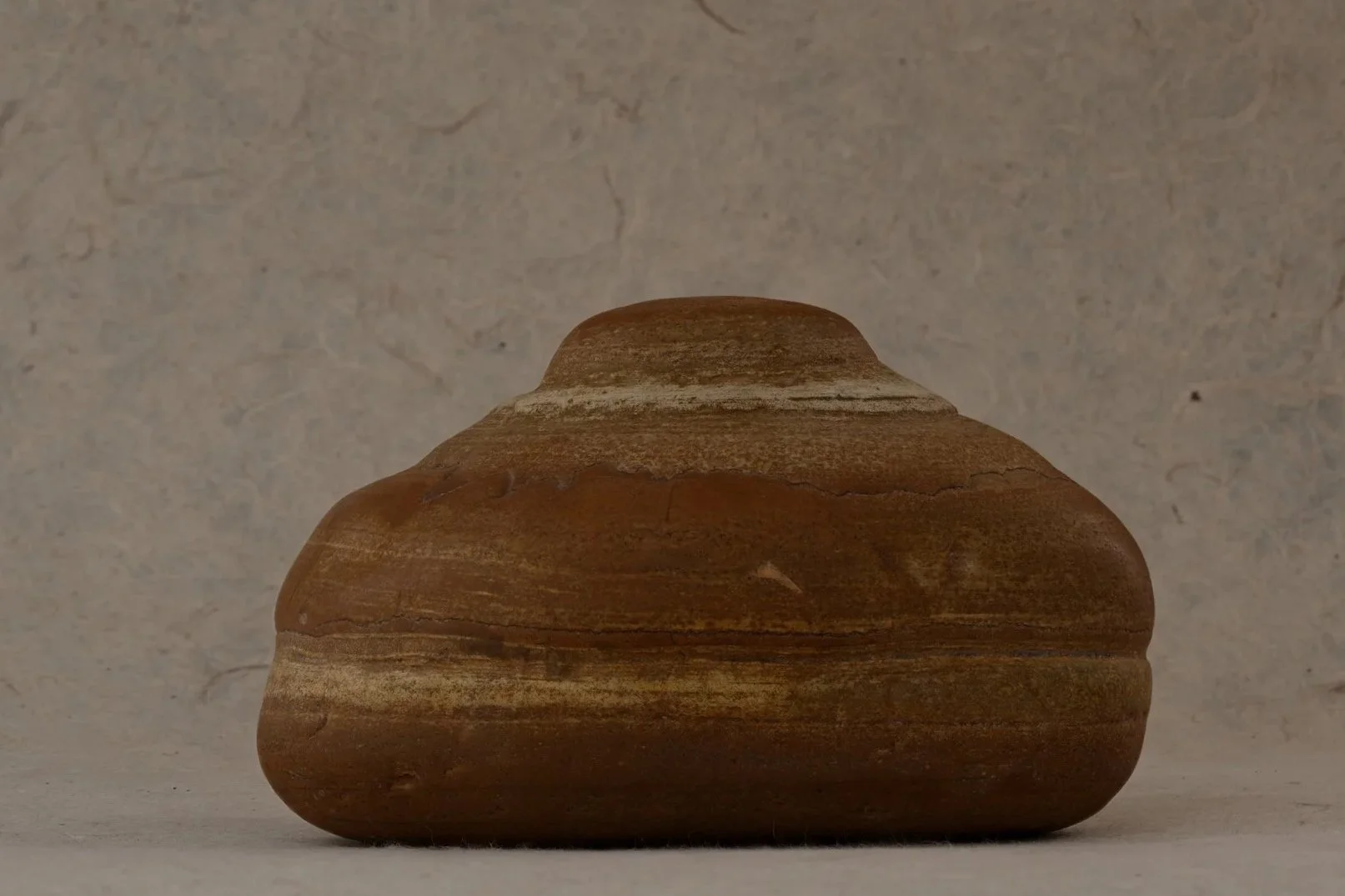 Close-up of a smooth, rounded, layered brown stone against a textured, light-colored background.