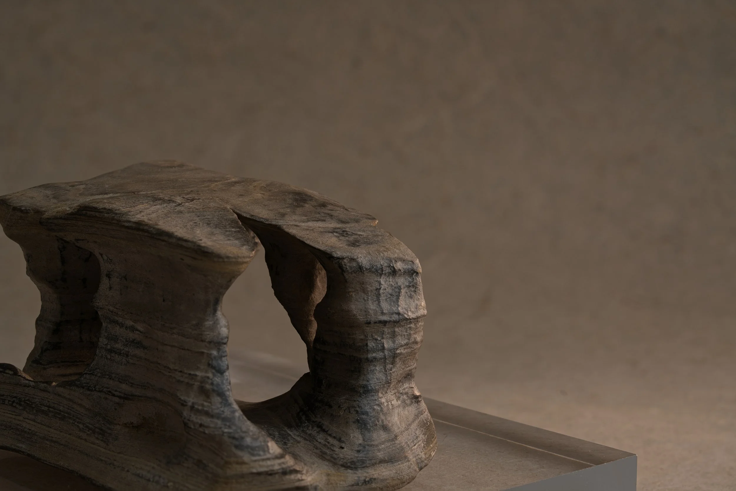 Close-up of a layered ancient ceramic vessel with a curving shape and textured surface, placed on a flat surface against a neutral background.