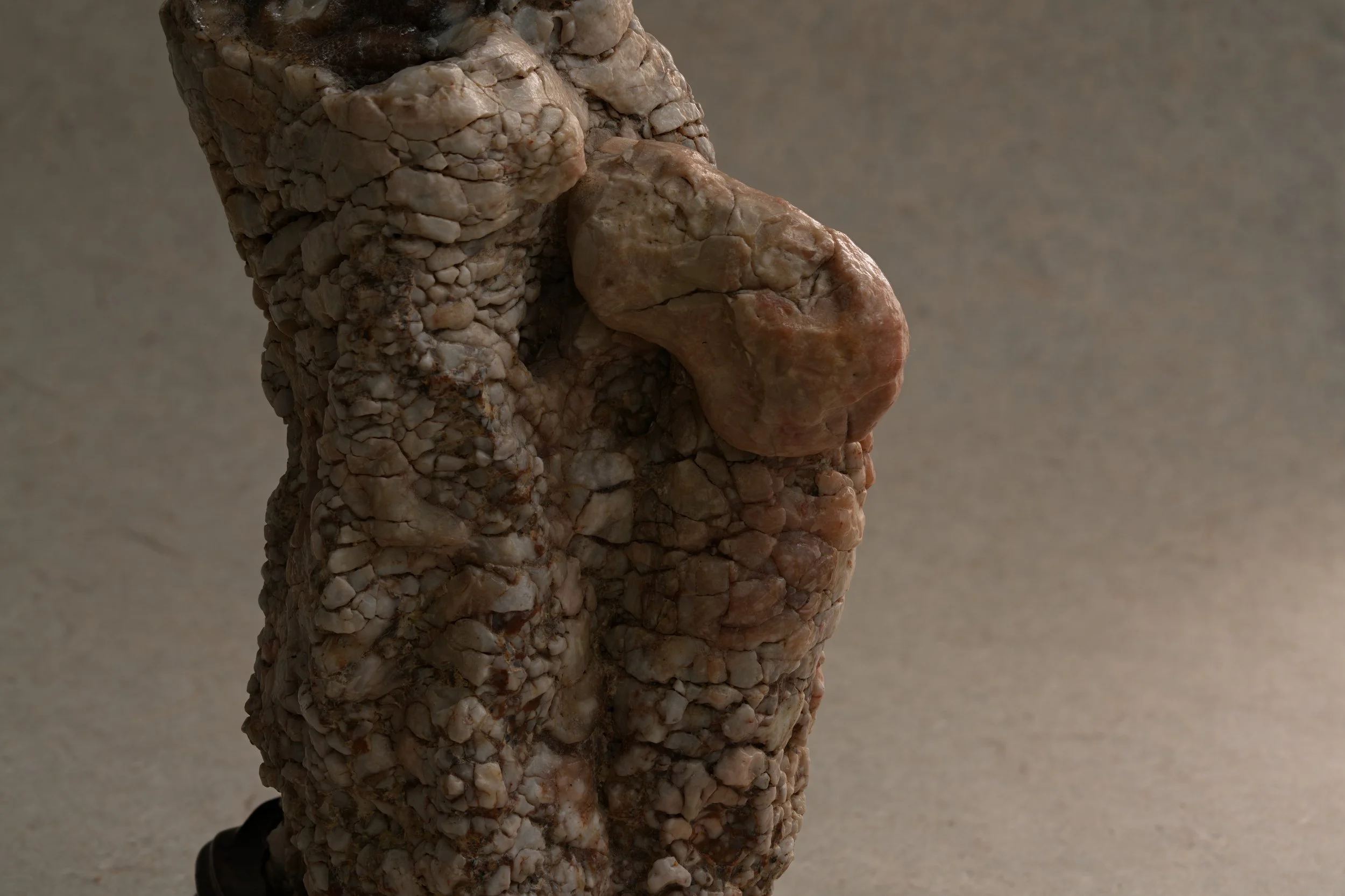 Close-up of a textured rock sculpture with an irregular surface featuring small, rounded stones embedded in a larger shape with a rough, natural appearance.