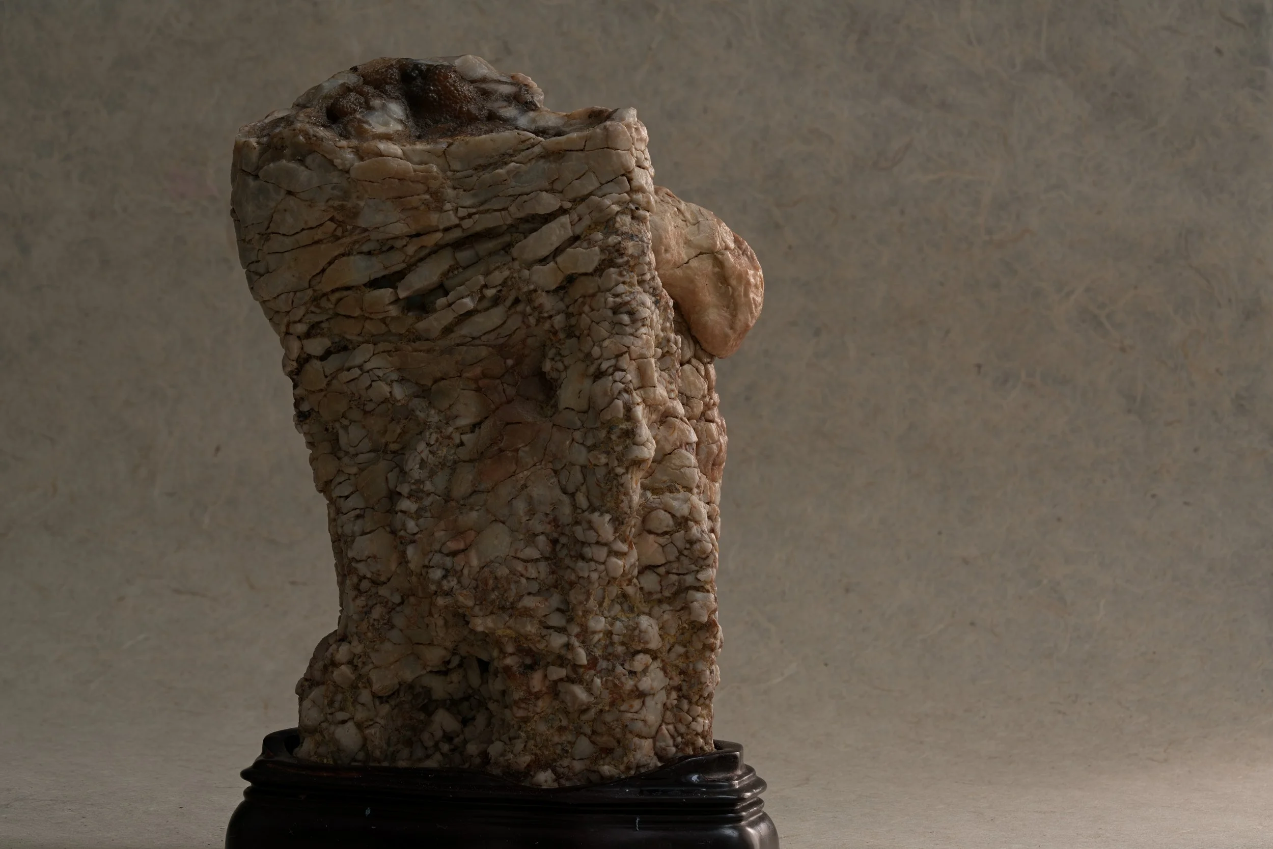 A sculpture made of small, coarse rocks, displayed on a black base against a plain background.