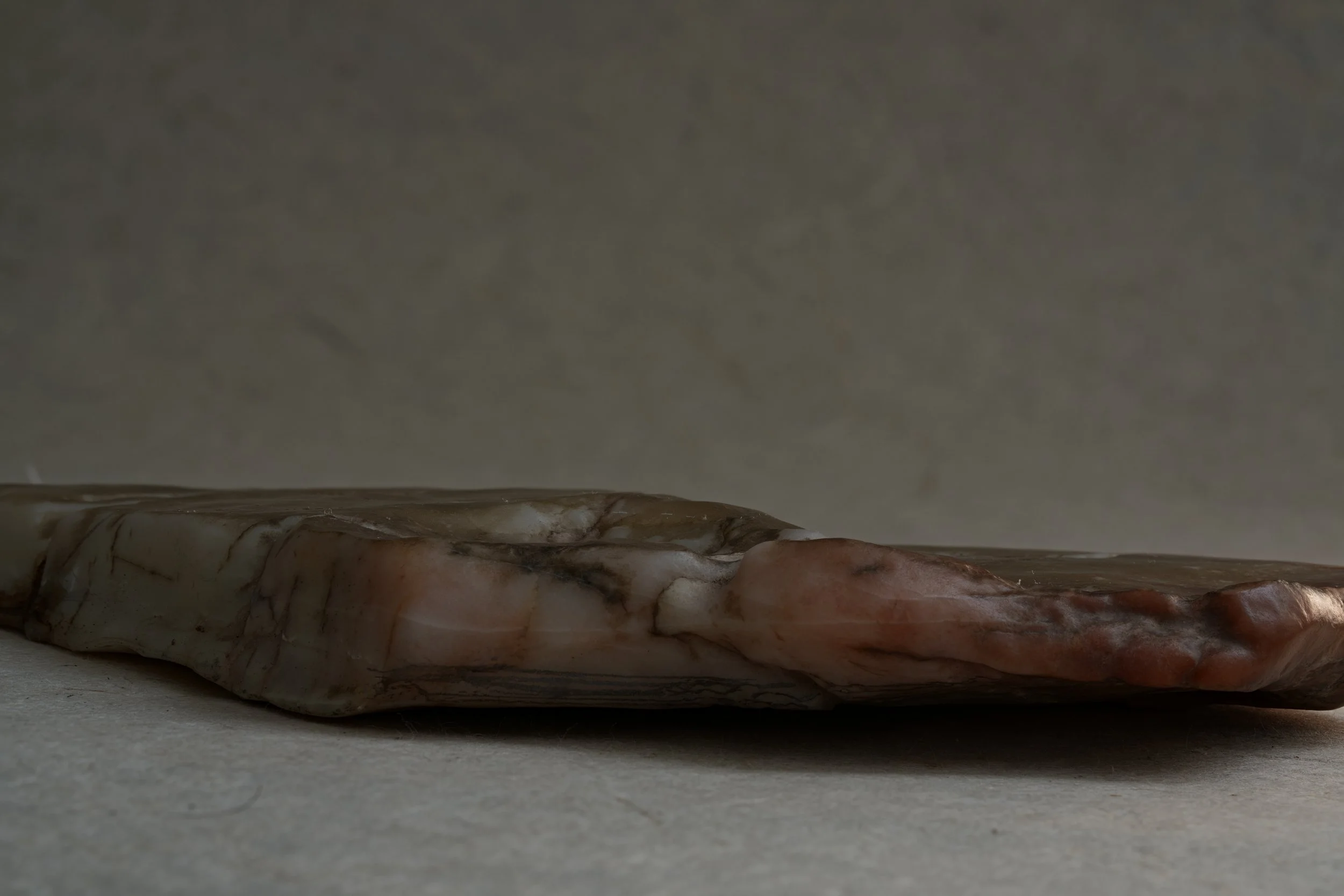 Close-up of a piece of polished marble with brown and white veins, lying on a light gray surface.