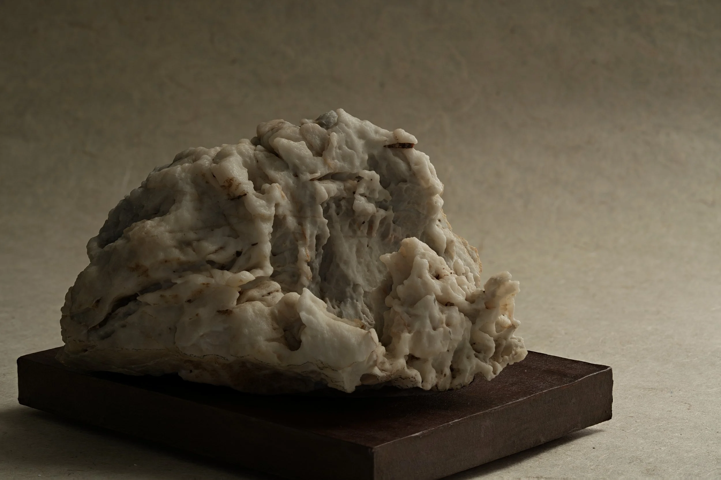 A large, textured rock on a black wooden base, with a neutral gradient background.