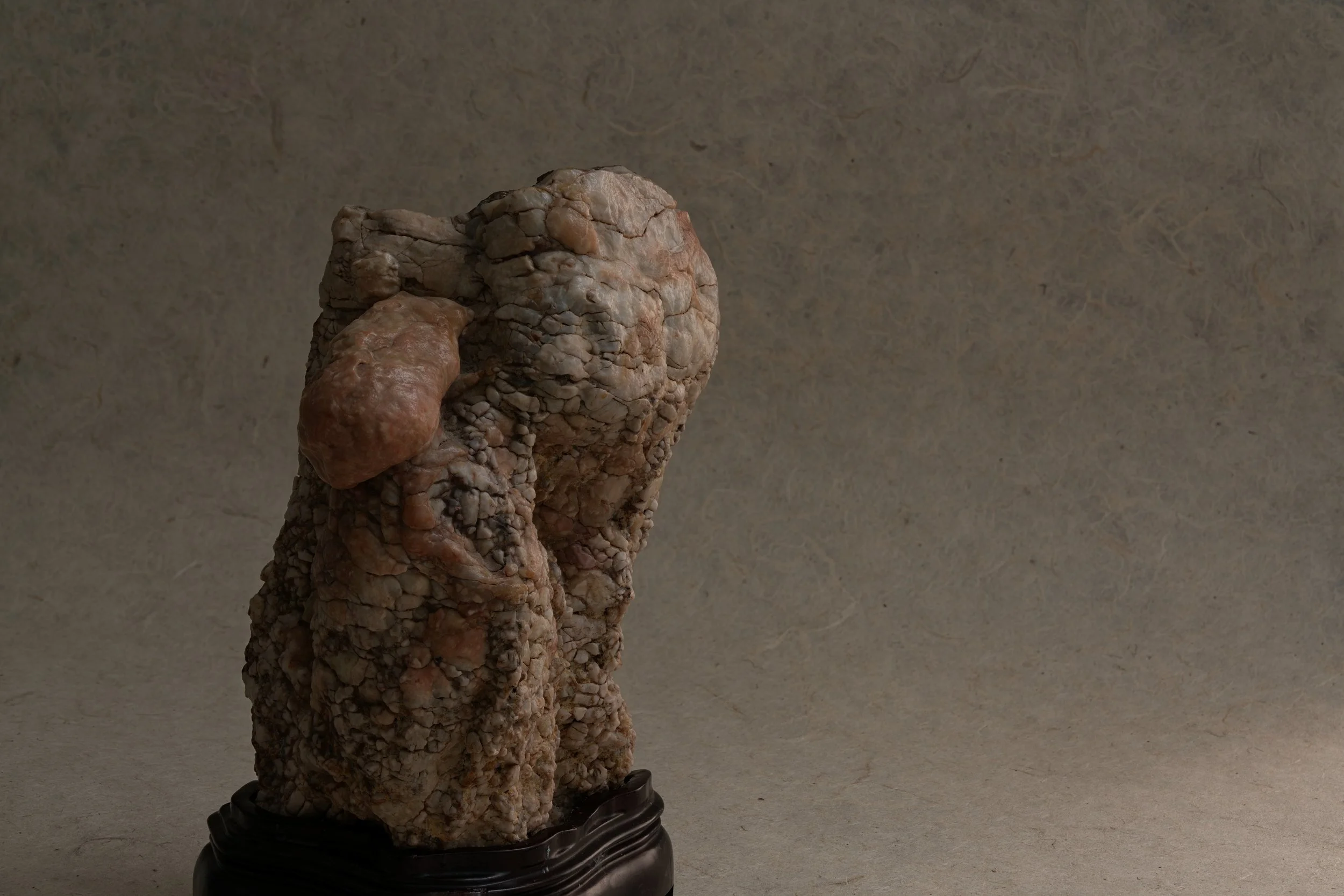 A sculpture resembling a human head and hand made from small stones or rocks, mounted on a black wooden base.