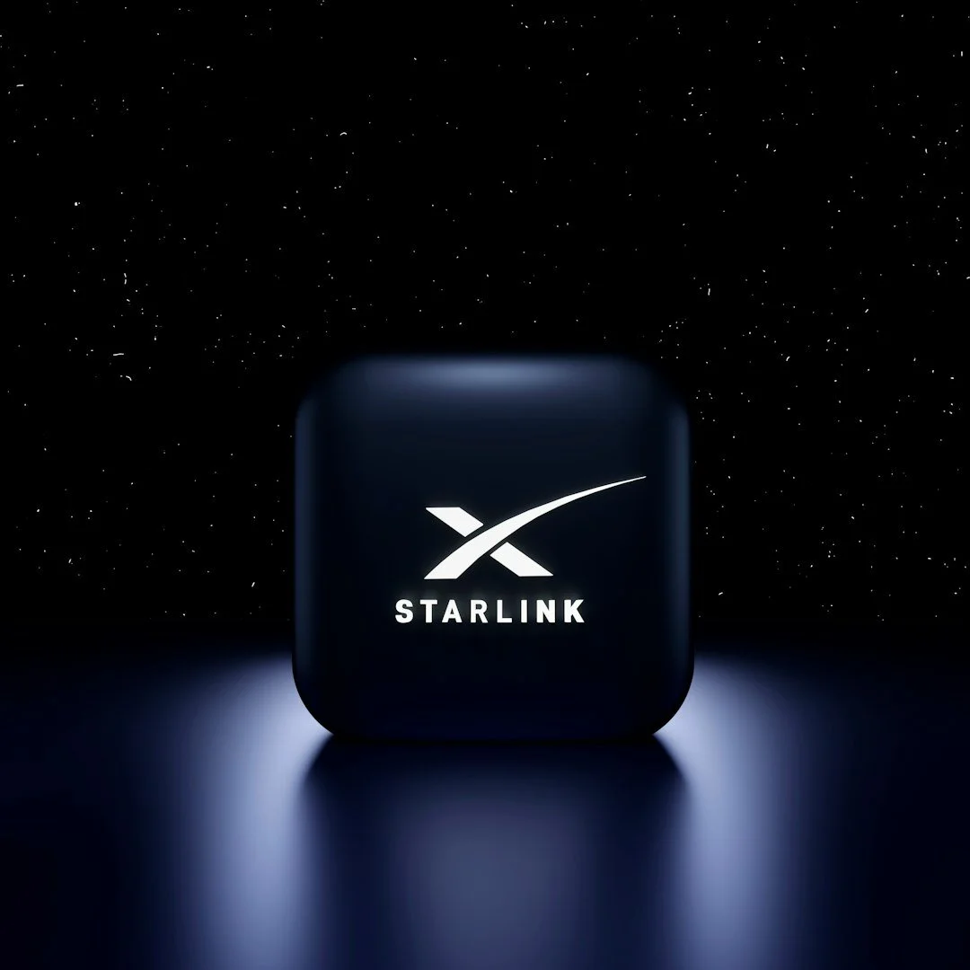 A black electronic device with a glowing starlink logo on it, set against a dark background with small white dots resembling stars.