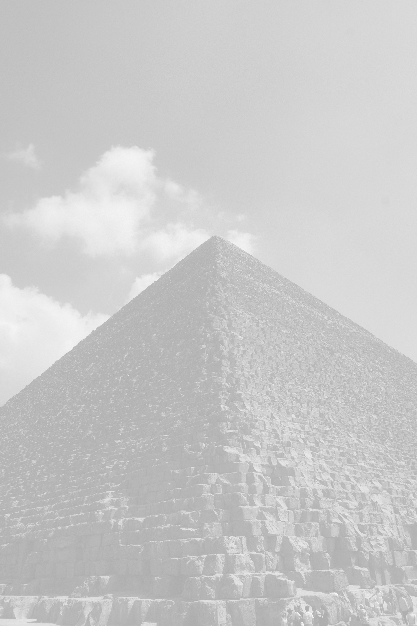 A black and white photograph of the Great Pyramid of Giza from a low angle, with a few tourists at its base.