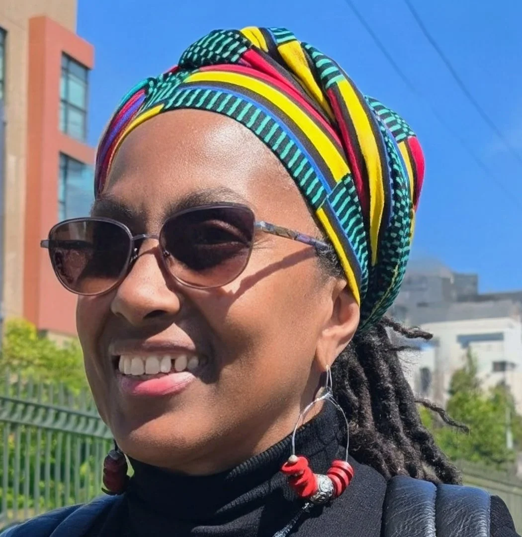Close-up of a smiling woman with glasses and natural curly hair.