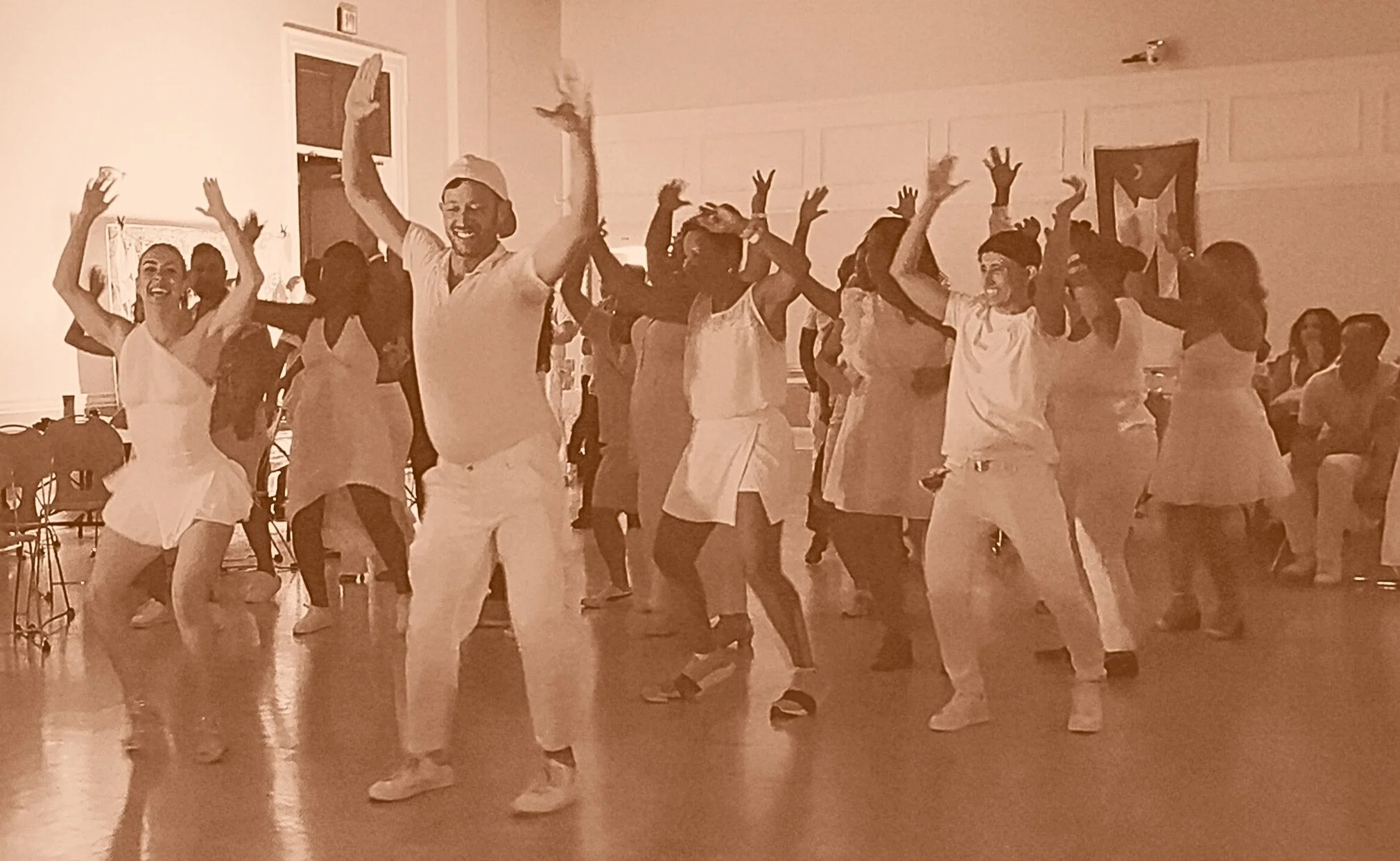 People dancing together in a room, all wearing white clothing, celebrating and having fun.