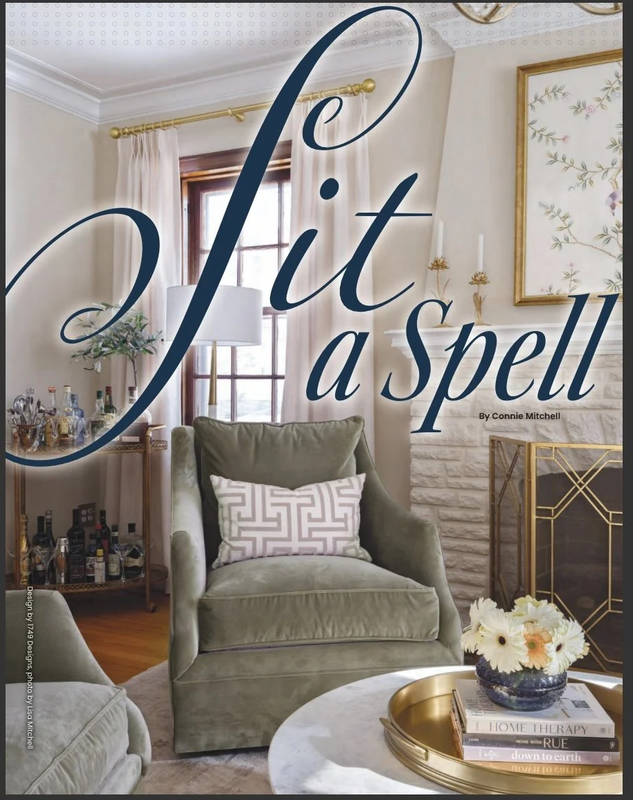 A cozy living room with natural light from a window, featuring green armchairs, a coffee table with a flower vase and books, a bar cart with bottles, and art on the walls. Overlaid text reads 'Slit a spell'.