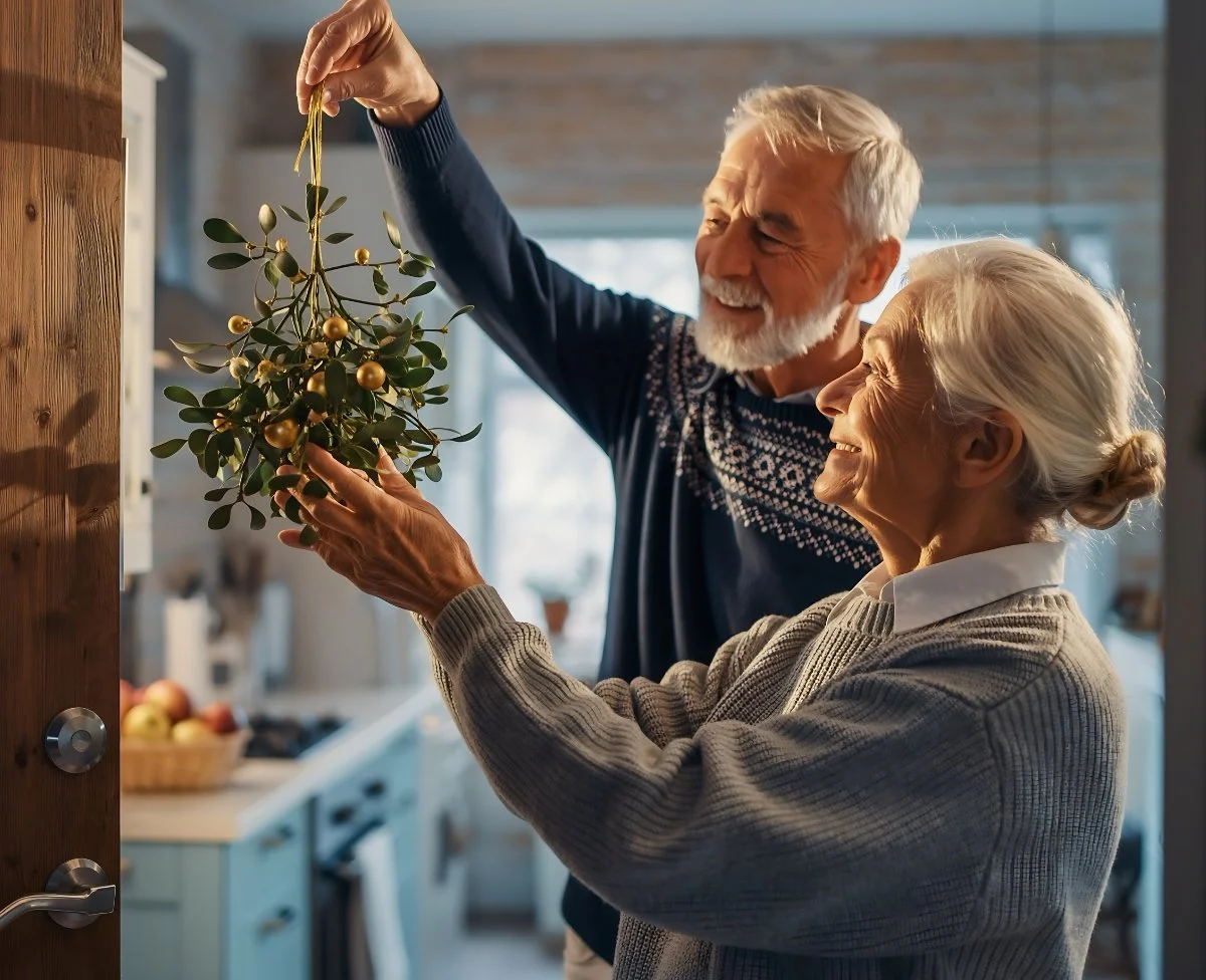 An elderly couple decorating a Christmas tree together in their kitchen.