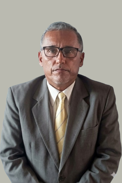 A middle-aged man with gray hair, glasses, wearing a gray suit, white shirt, and a yellow tie, standing against a plain background.