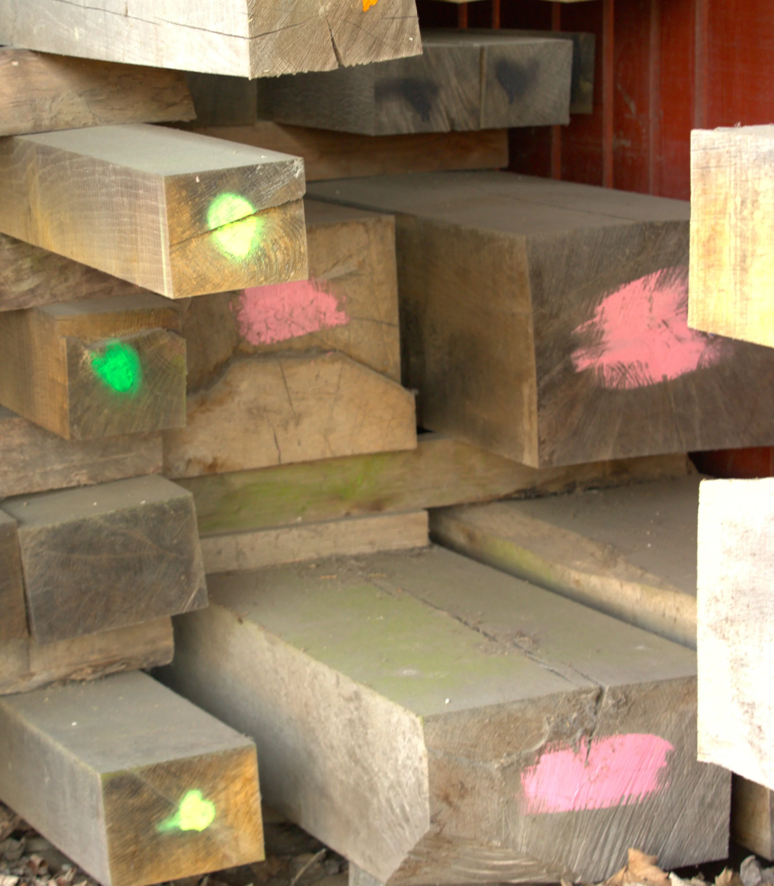 Stacked lumber inside a wood workshop with a wooden fence and wall in the background.