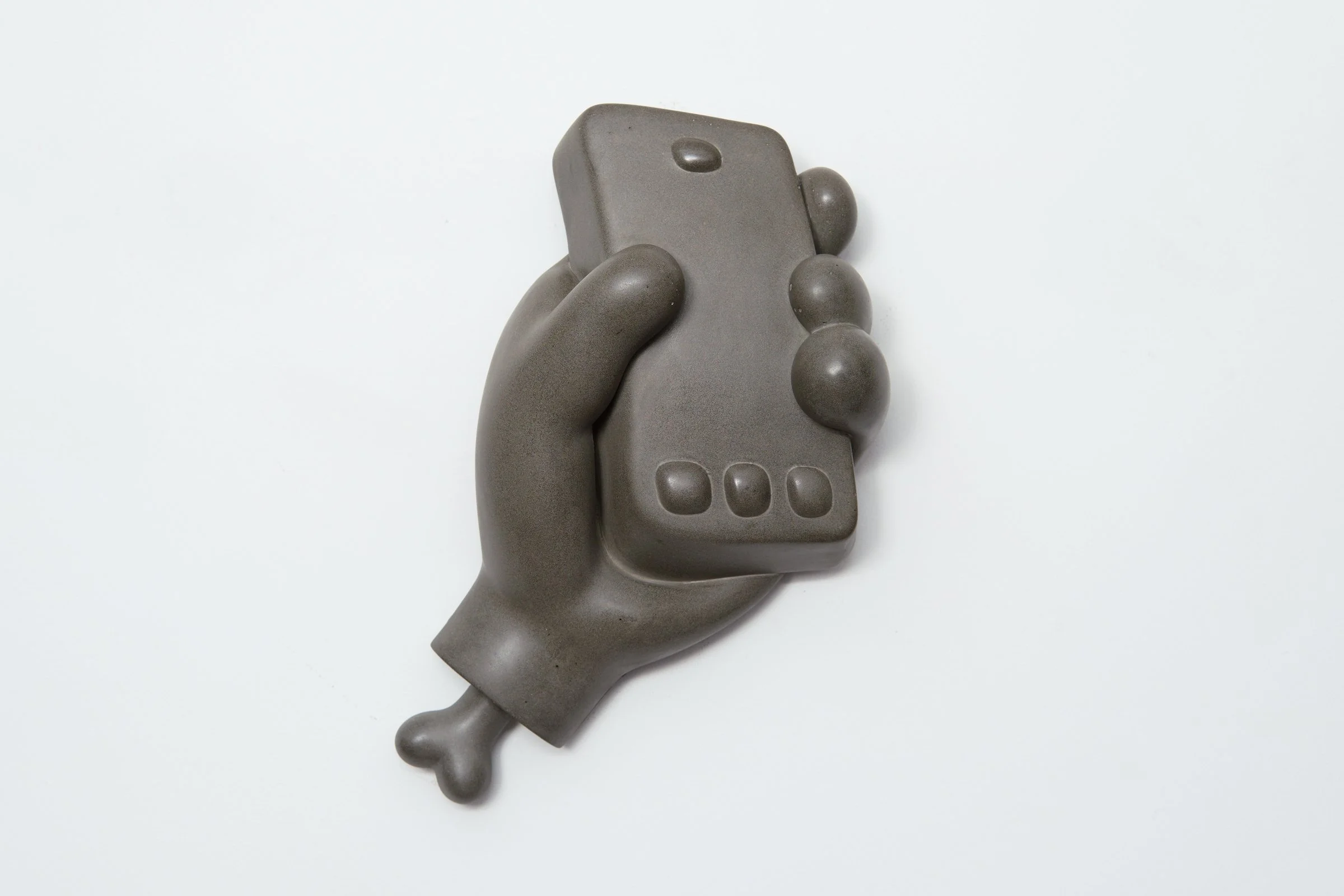 Jamie Howlett sculpture; polished cement hand gripping digital device, featuring truncated wrist and visible bone fragment. Meditation on intersection of human anatomy and artifice