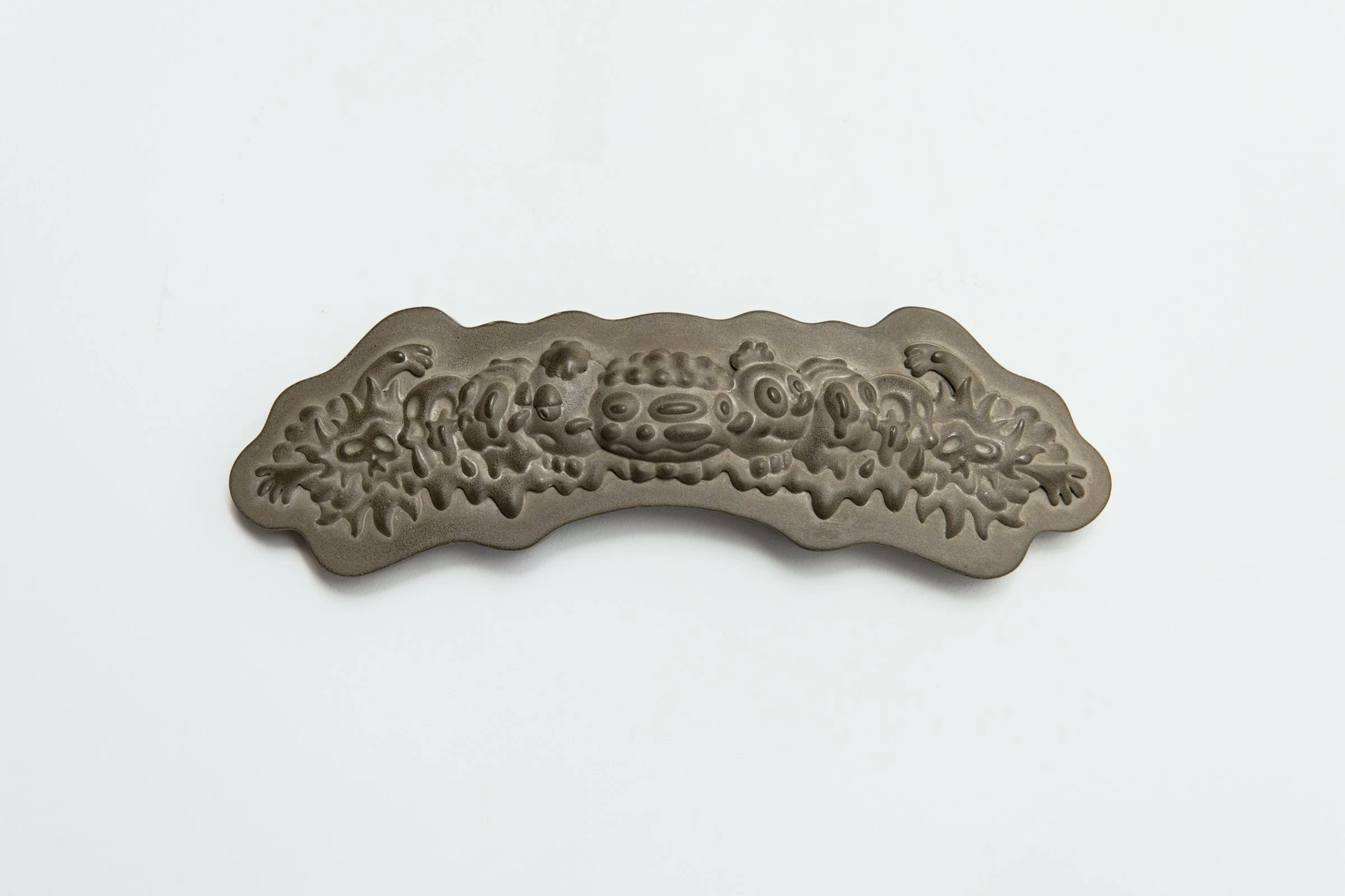 Jamie Howlett sculpture; horizontal relief frieze cast in polished cement and flint. Linear arrangement of undulating, cartoon-inspired forms interrogating material weight and cultural dissonance