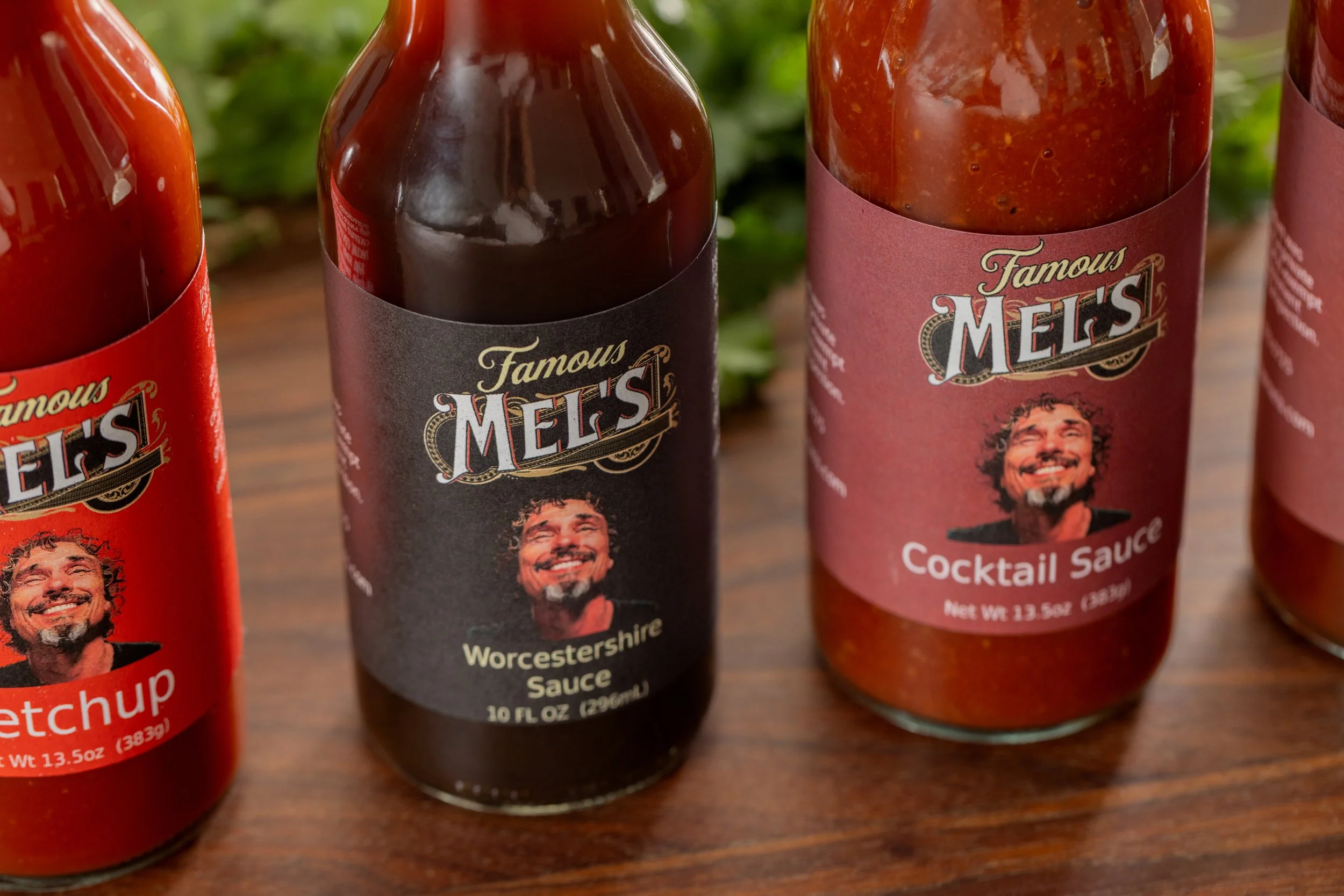 Three bottles of Mel's barbecue sauces, including Worcestershire Sauce and Cocktail Sauce, on a wooden surface.