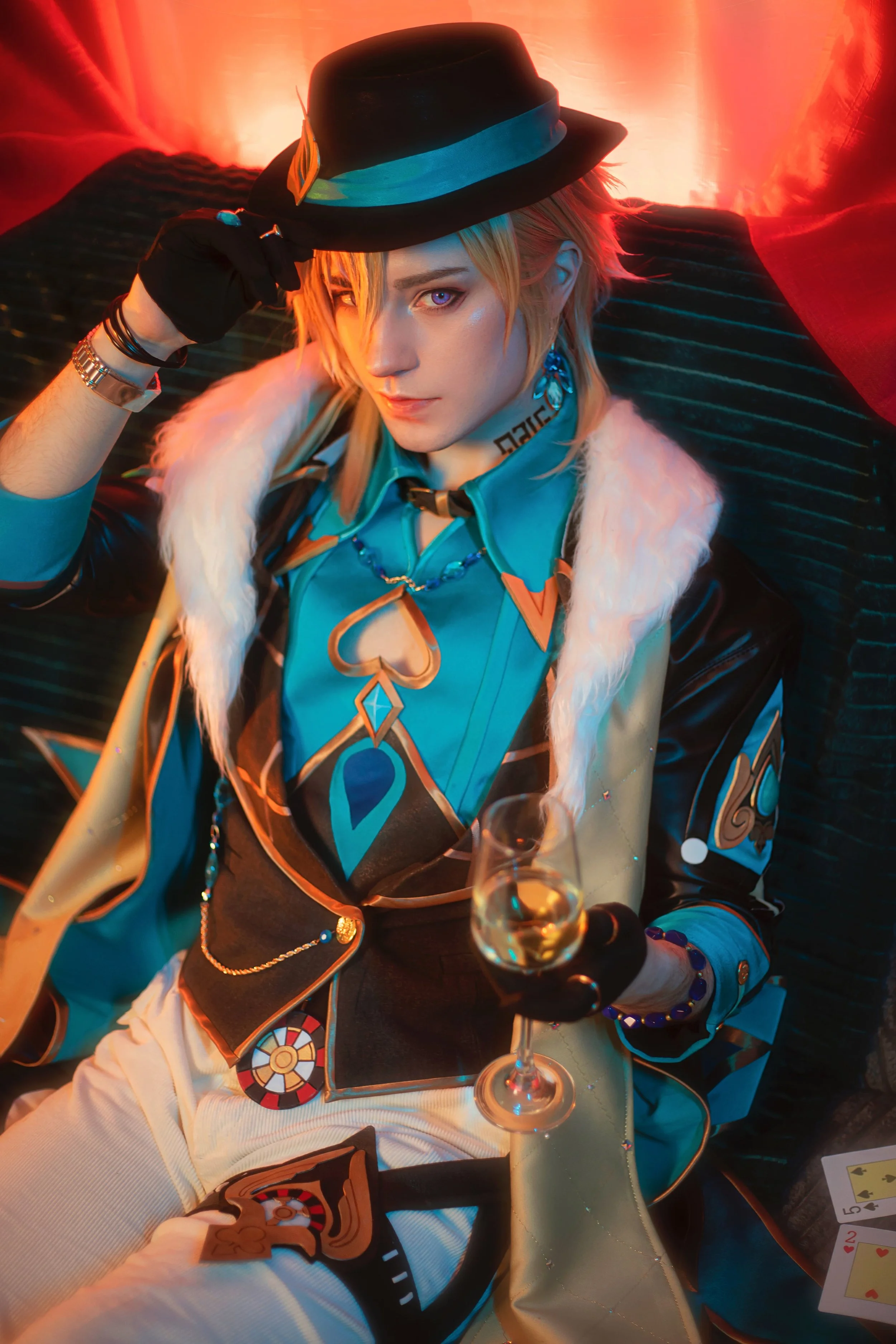 A person in a colorful costume, holding a glass of wine, sitting on a dark bed with a red backdrop.