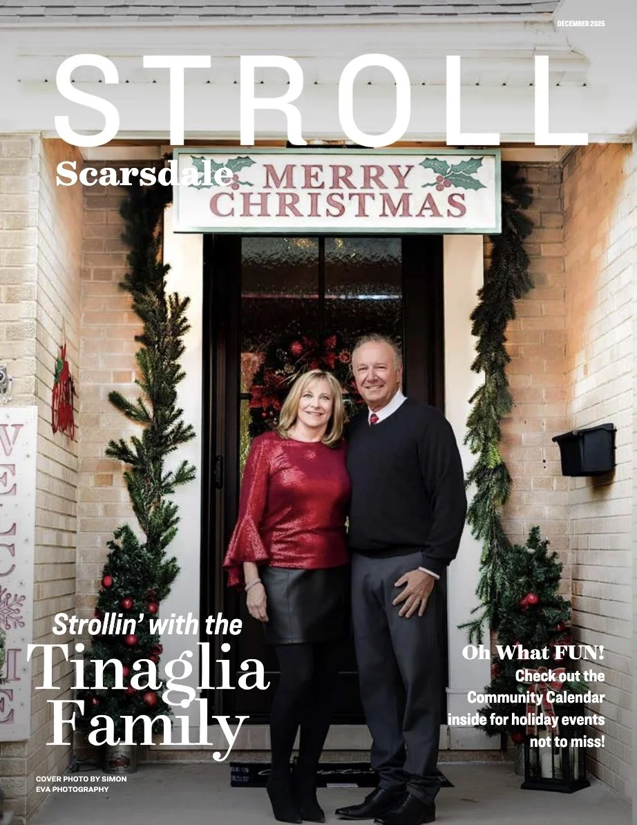 A couple standing in front of a door decorated for Christmas, with a 'Merry Christmas' sign above, Christmas garlands framing the doorway, and small Christmas trees decorated with red ornaments on either side.