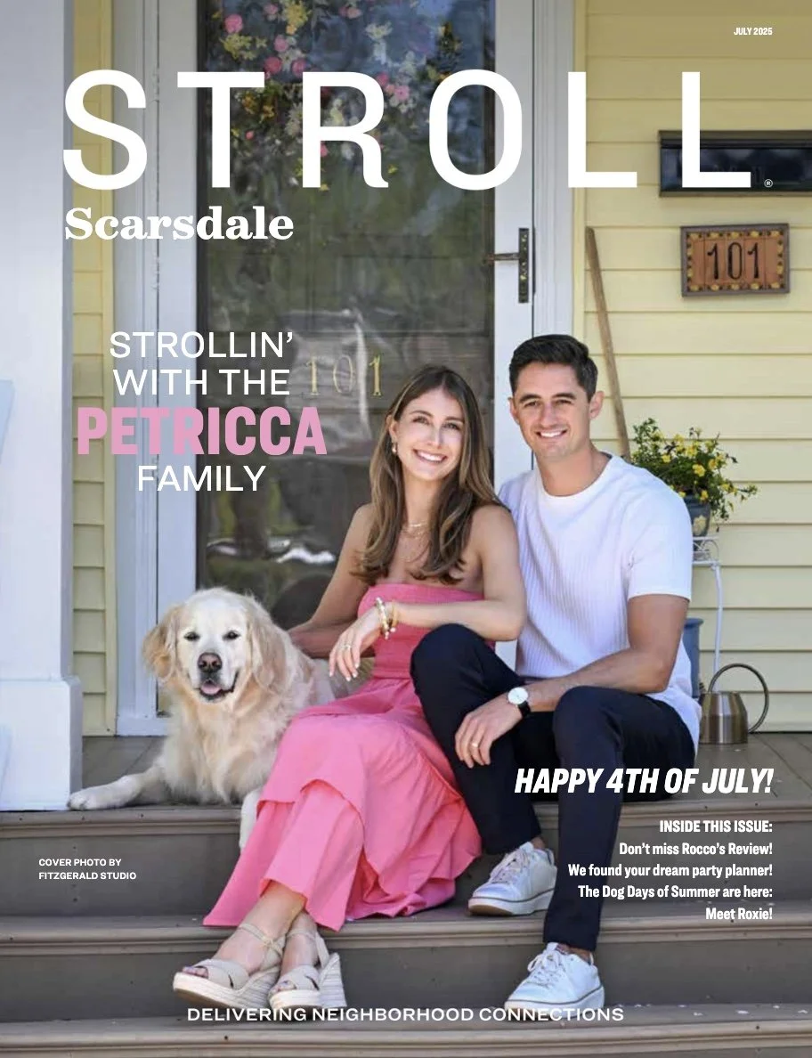 Cover of Stroll Scarsdale magazine featuring a smiling woman in a pink dress, a smiling man in a white shirt, and a golden retriever sitting on the front porch of a yellow house with a door, house number 101, a potted plant, and a garden tool, celebrating the 4th of July.