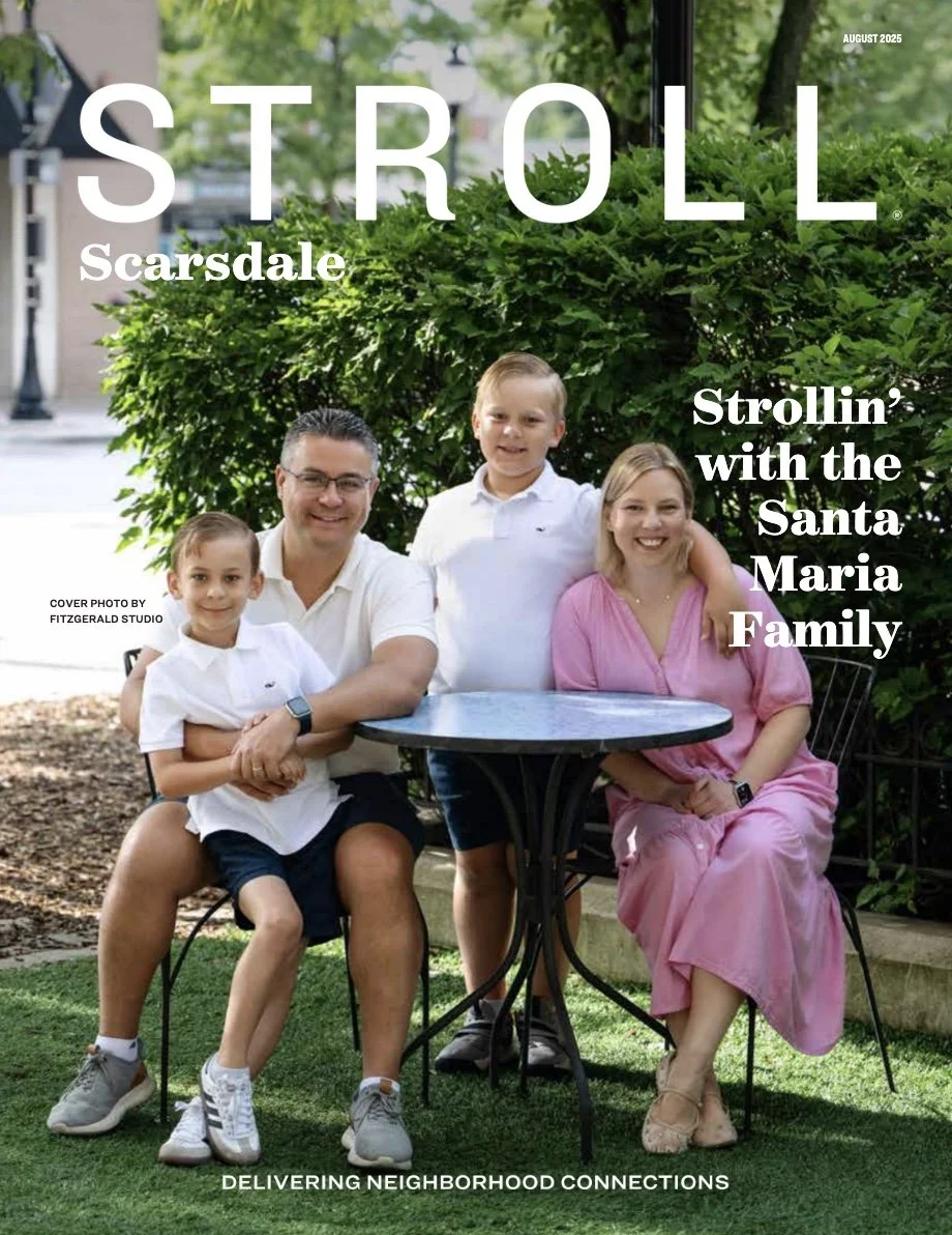 A family of four sitting outside at a round table, smiling. The father and son are wearing white shirts, the mother is dressed in pink, and the older son is in a white polo. They are sitting on chairs on a grassy area with bushes and trees behind them, and a sidewalk and building in the background. The image includes text indicating it is the August 2025 issue of 'Stroll' magazine, themed around neighborhood connections, with a cover photo credit to Fitzgerald Studio.