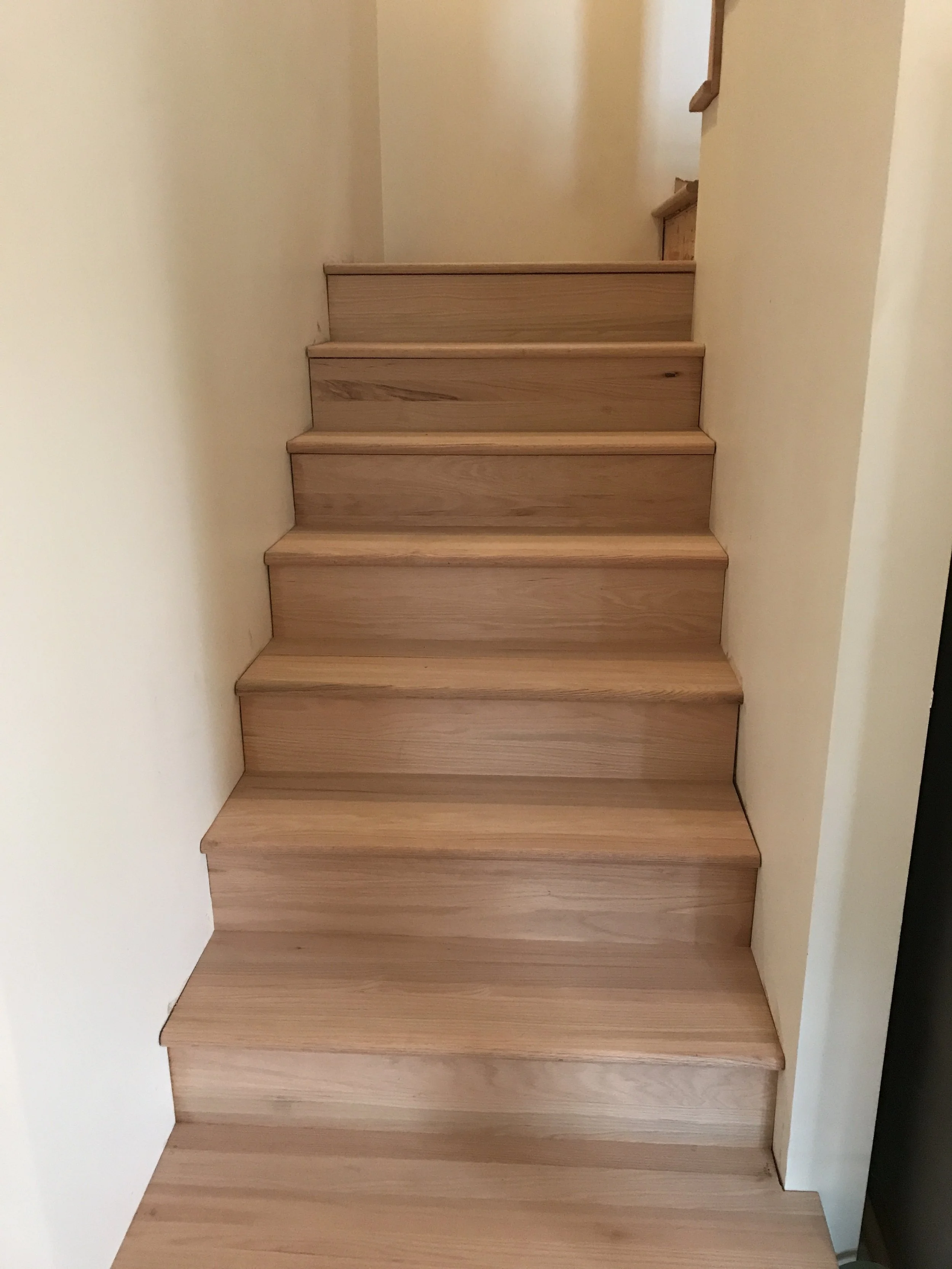 Wooden staircase with five steps, surrounded by cream-colored walls, leading upward to a higher floor.