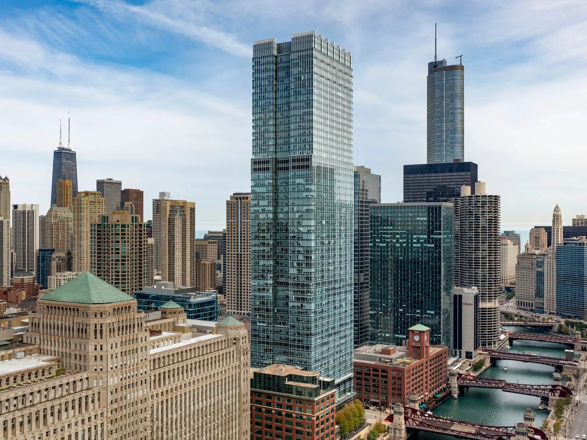 Skyscrapers in downtown Chicago with the Chicago River and bridges in the foreground, under a partly cloudy sky.
